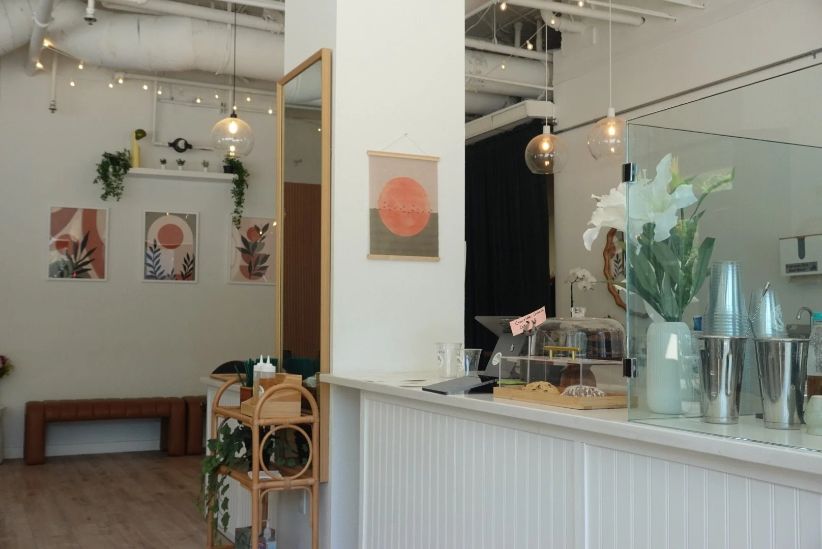 Interior of a modern cafe with white walls, artwork, and a flower display on the counter, featuring minimalist decor and warm lighting.