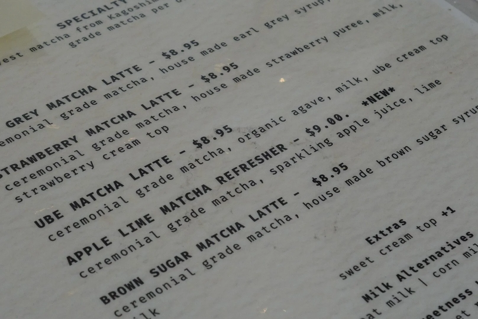 Close-up of a cafe menu listing matcha lattes, strawberry matcha, apple lime matcha, and brown sugar matcha, with prices and descriptions.