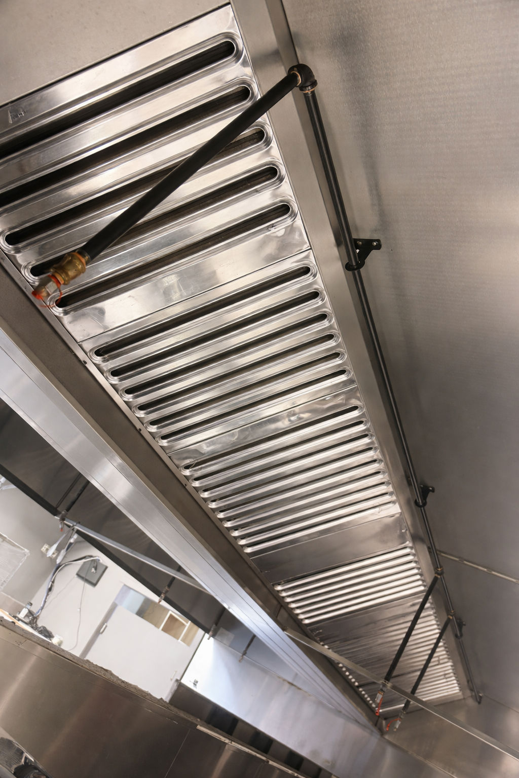 Close-up of a commercial kitchen stainless steel exhaust hood with black suspension rods and a metal grill.