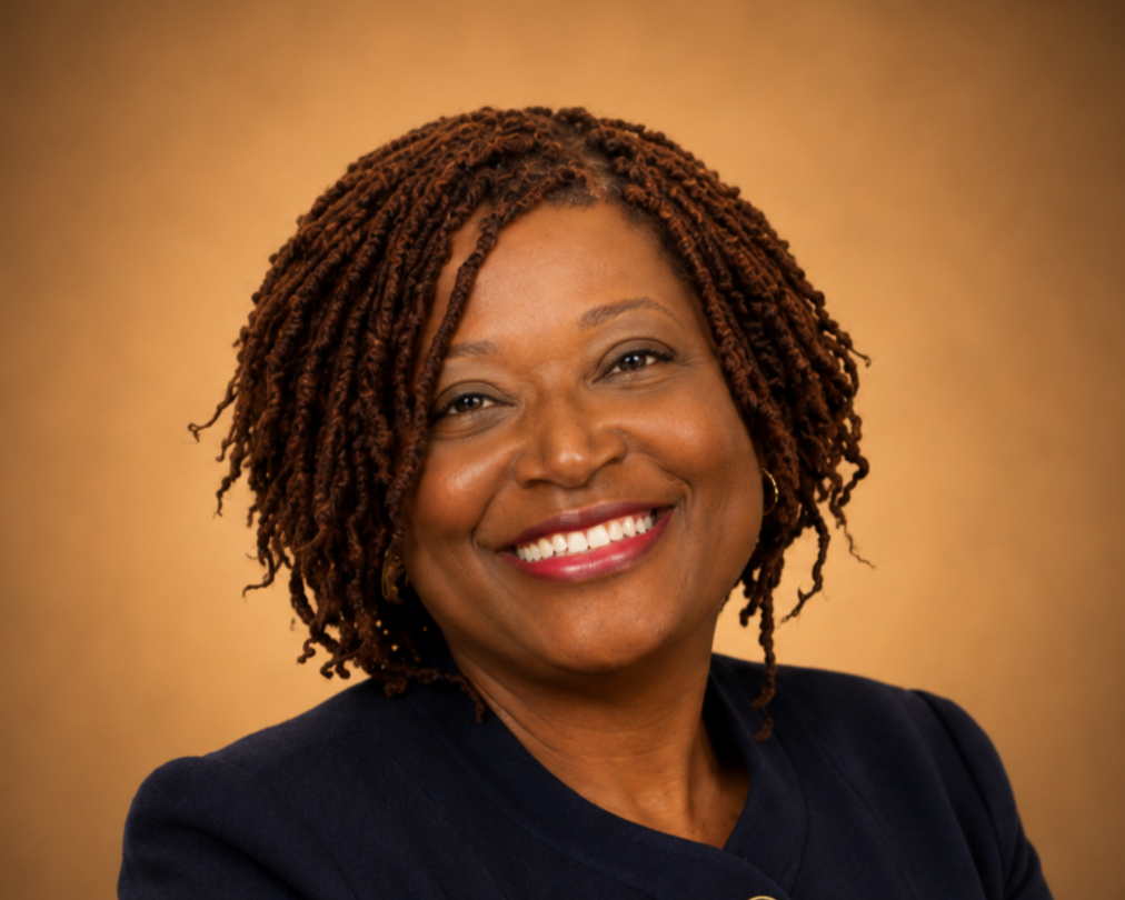 A smiling African American woman with curly, shoulder-length hair, wearing a navy blazer, against a warm brown background.
