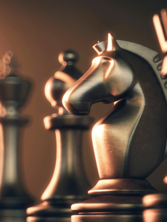 Close-up of metallic chess pieces, including a knight in focus, with warm lighting.