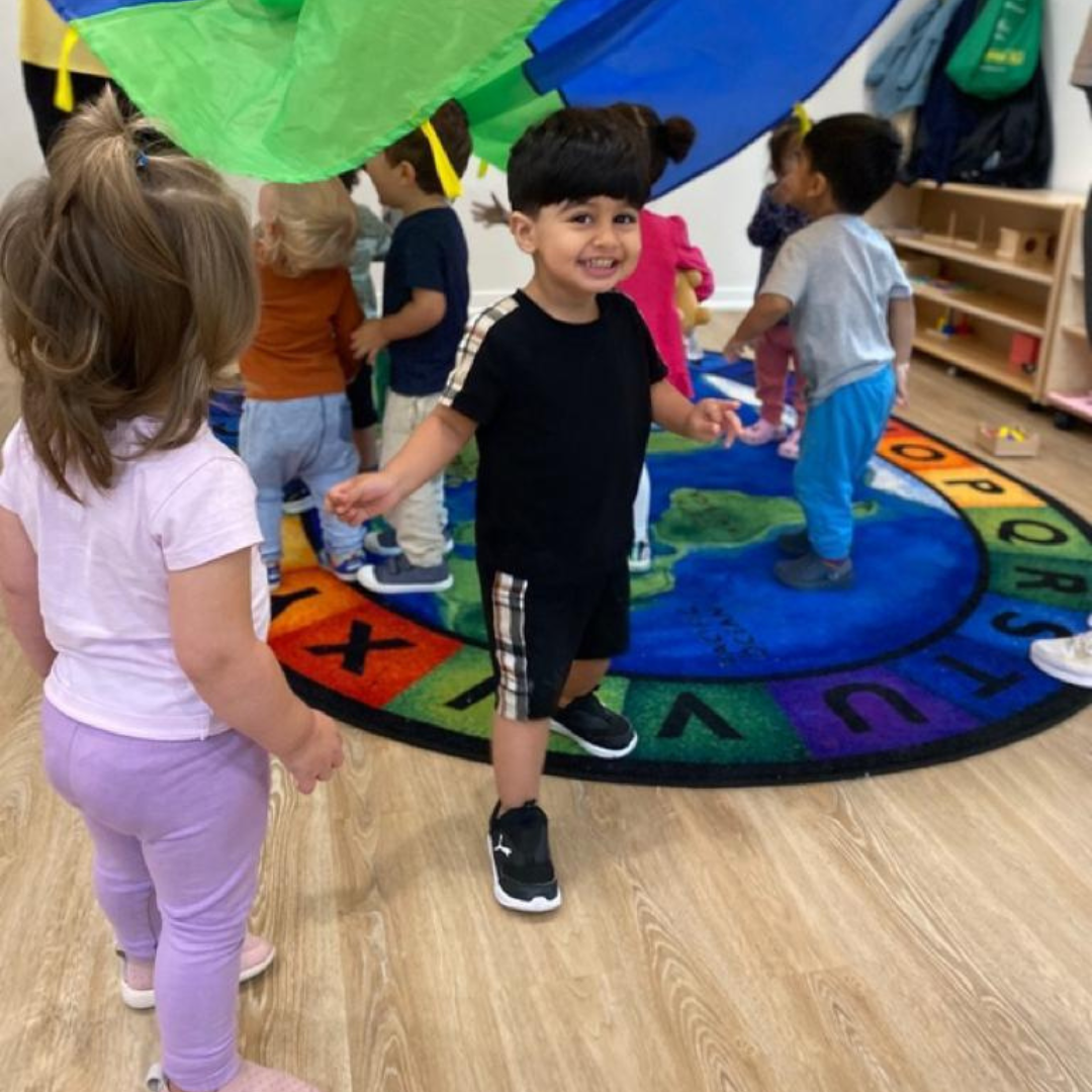 A group of young children playing on a colorful, circular, educational rug with numbers and letters in a classroom.