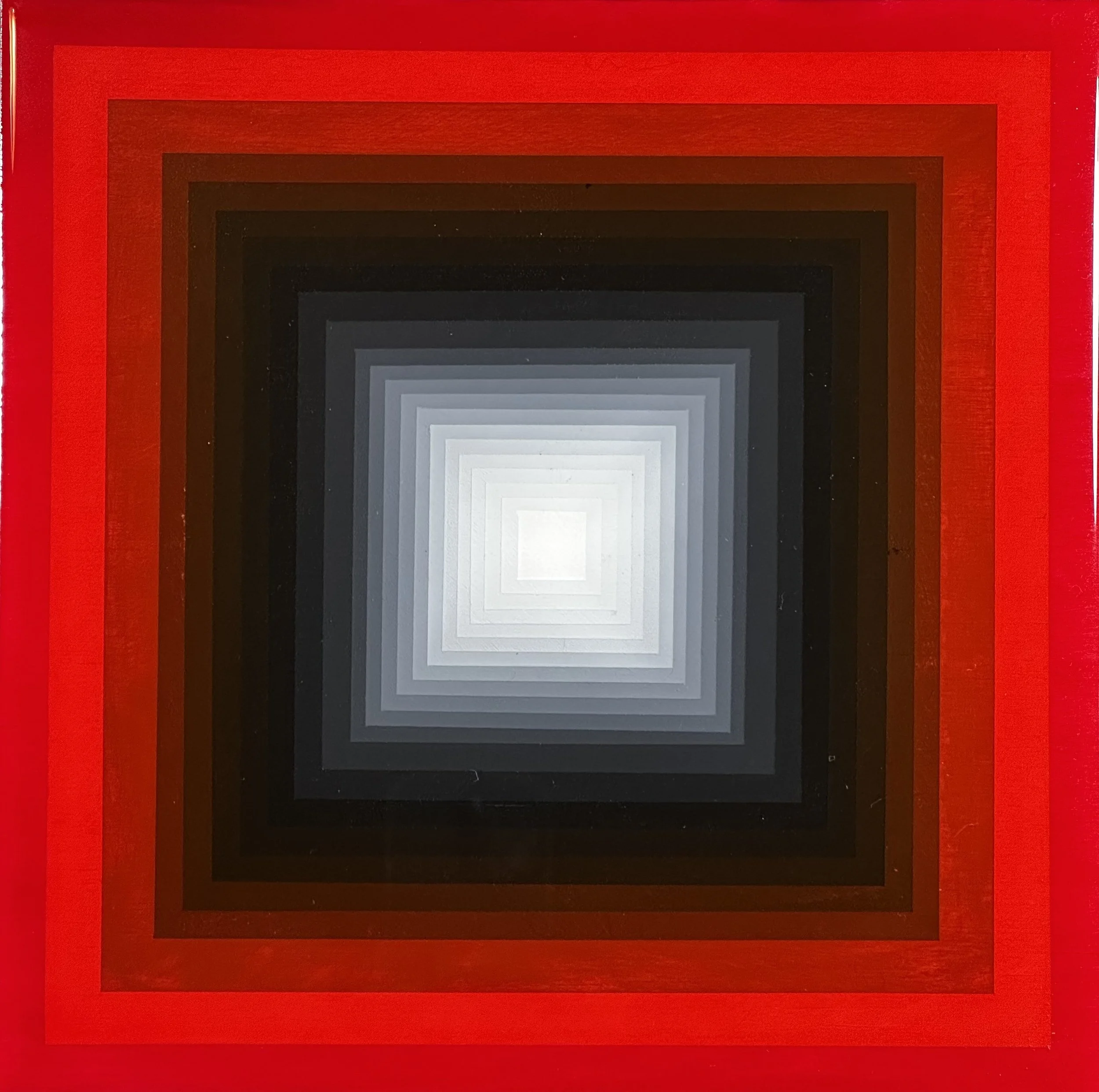 A rectangular object with concentric squares in shades of red, black, gray, and white, creating a tunnel-like visual effect.