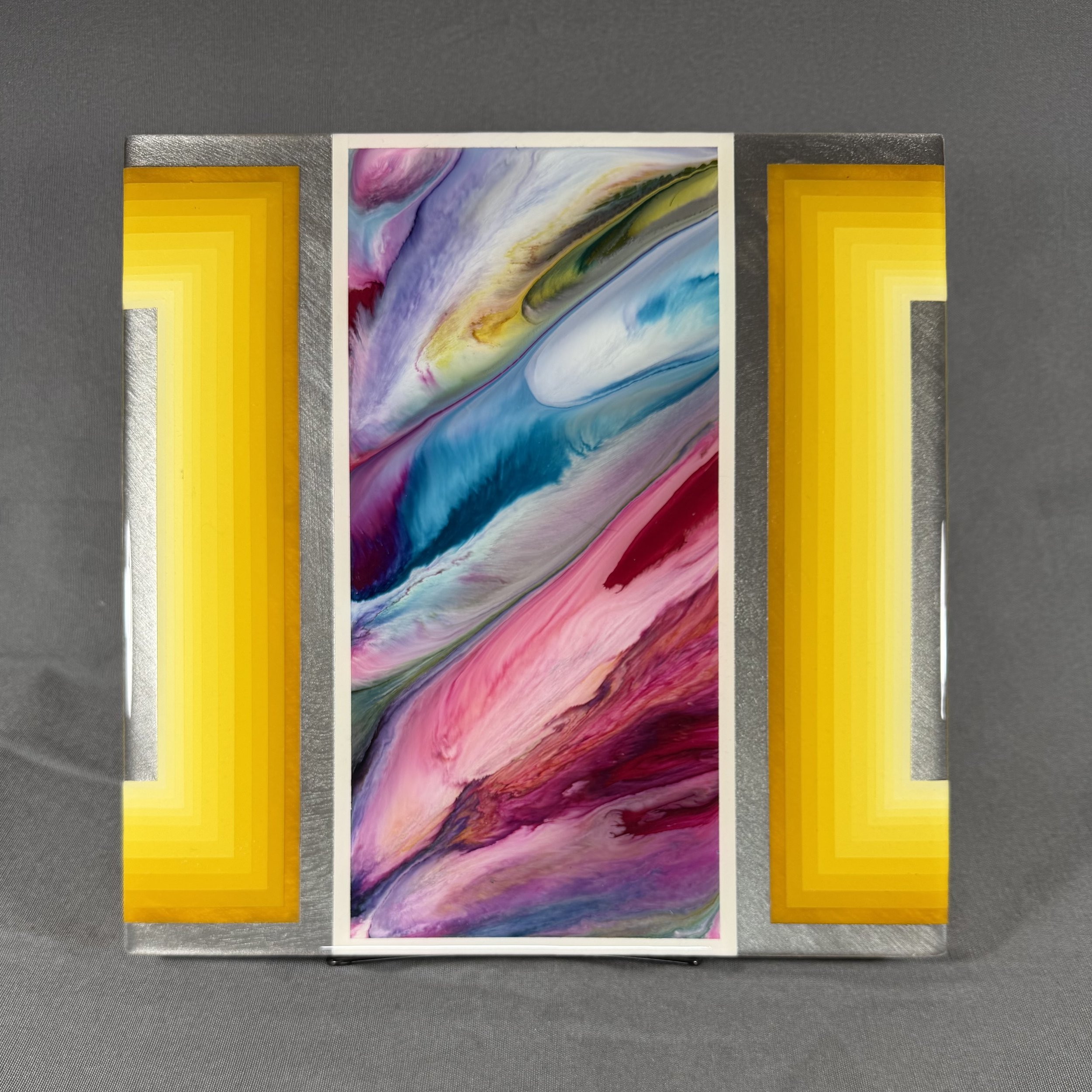 A colorful abstract painting with swirls of pink, purple, blue, green, yellow, and white, displayed on a wall with gray background and yellow panels on each side.