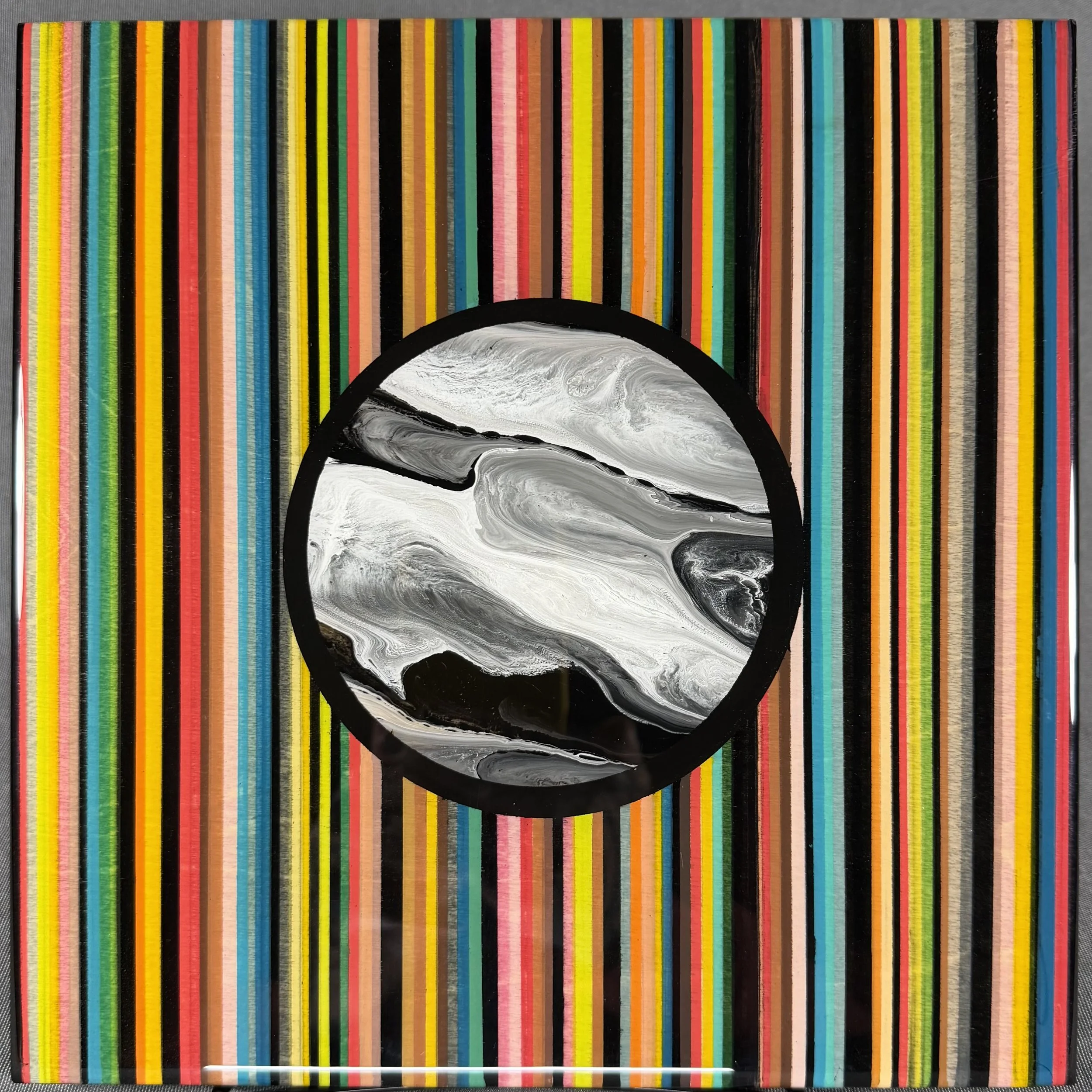A colorful collection of straight and textured strips arranged vertically across the entire image with a black circle near the bottom. The strips are in various bright colors like pink, yellow, green, blue, red, orange, and brown.