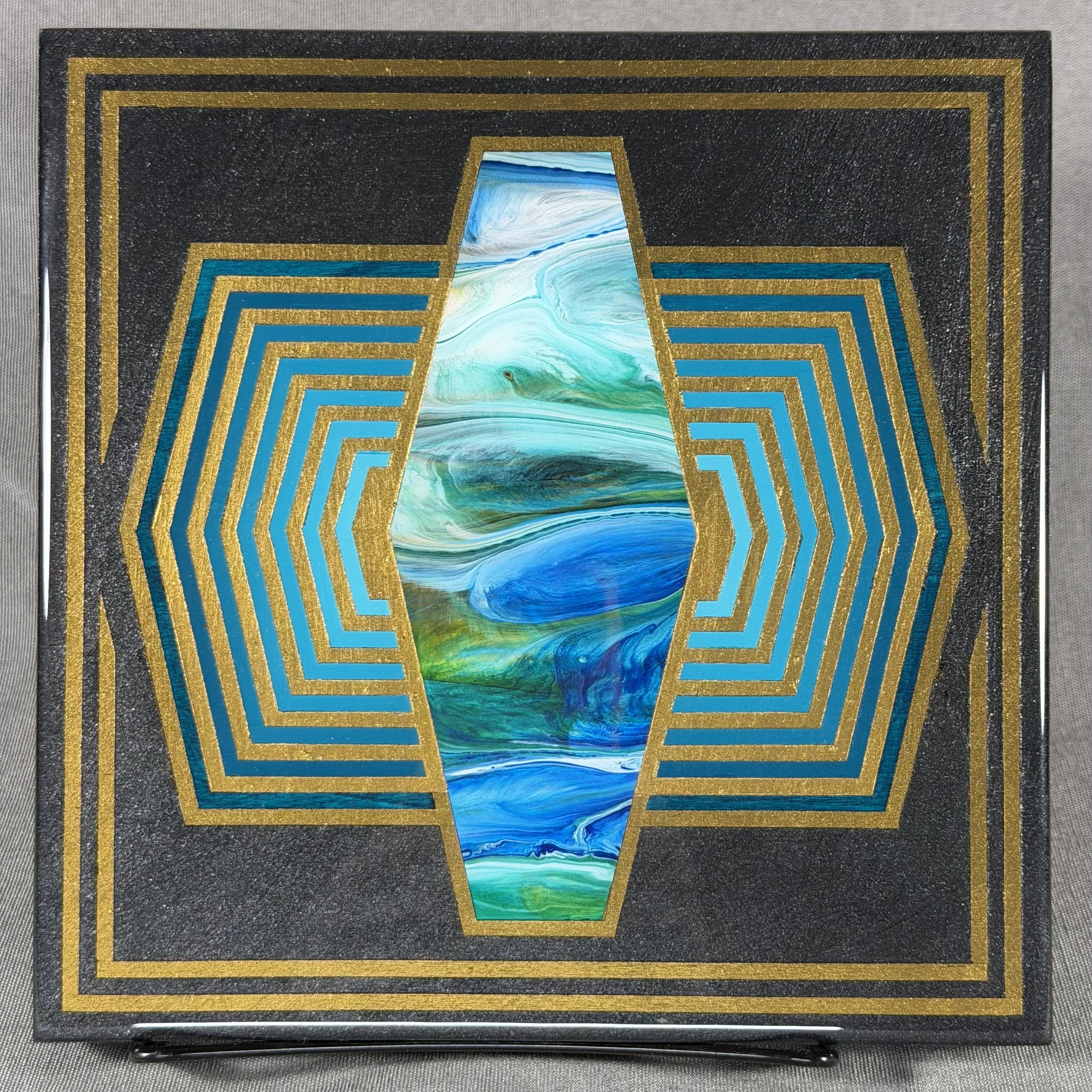 A black rectangular box with gold and blue geometric designs, and an abstract, colorful, marble-like painting in the center.