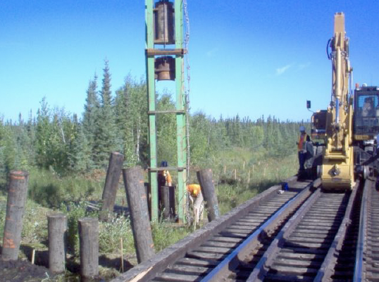 Construction workers installing or repairing railroad tracks with construction machinery on a sunny day in a rural area.