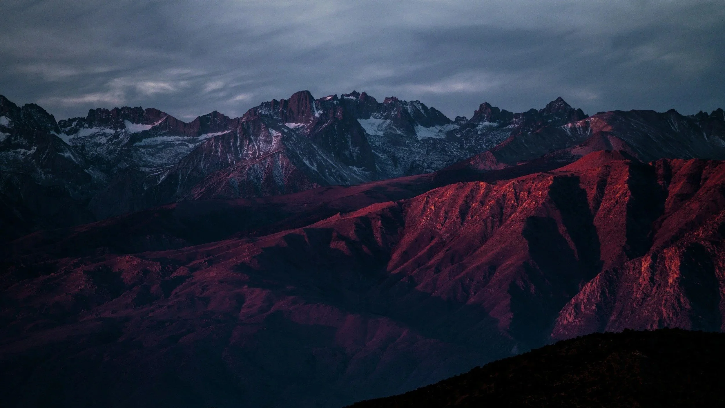 Mountain range during sunset with snow-capped peaks and reddish-brown lower slopes.