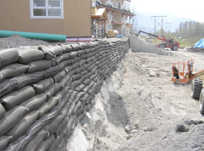 Construction site with a retaining wall made of gravel bags, machinery, and partially completed building in background.