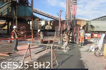 Workers wearing safety vests and helmets working on a construction site with orange barriers and heavy machinery.