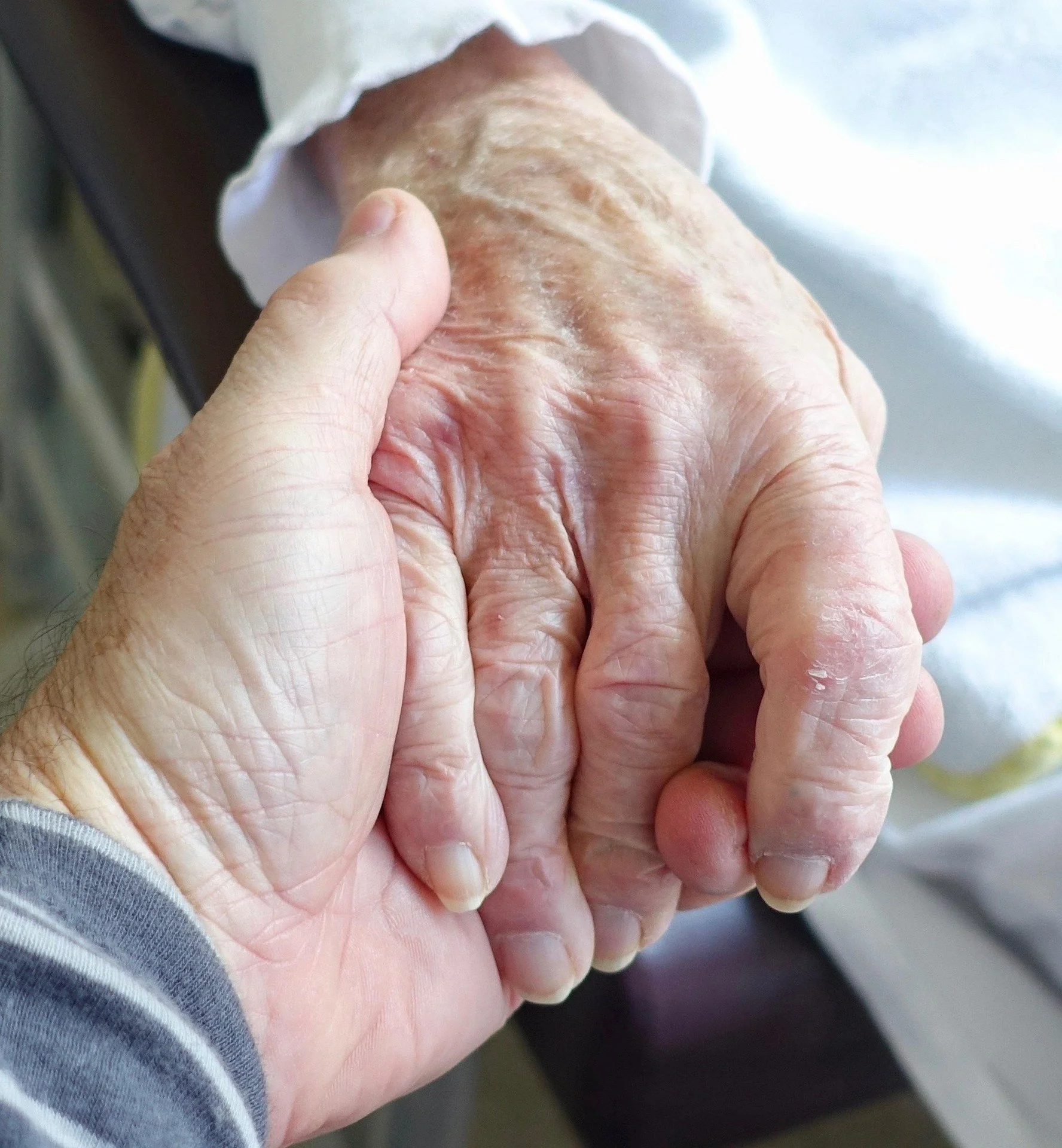 Close-up of two wrinkled hands clasped together, possibly indicating comfort, support, or unity.