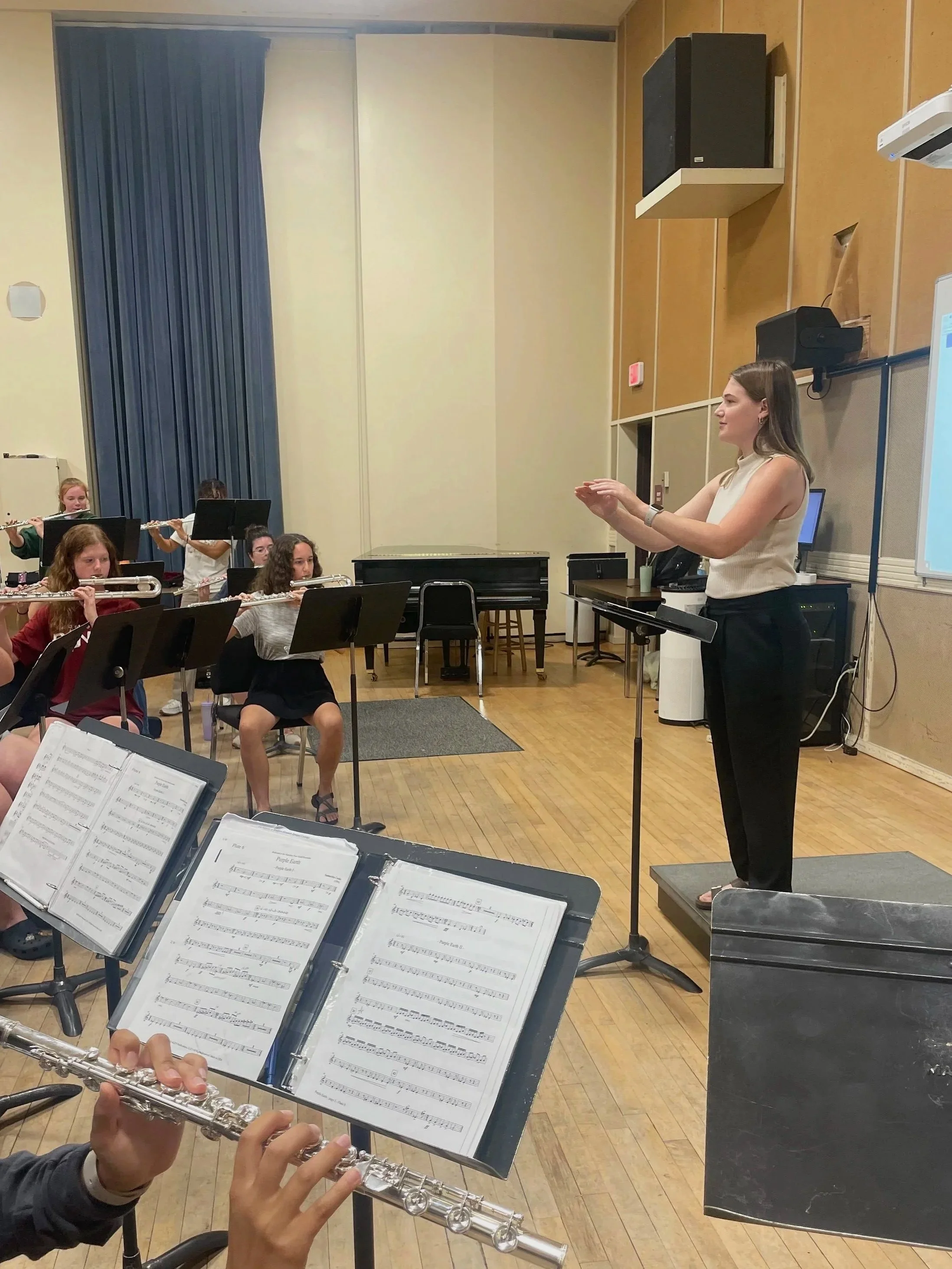 Lindsey Kovach conducting a flute ensemble in a rehearsal room.