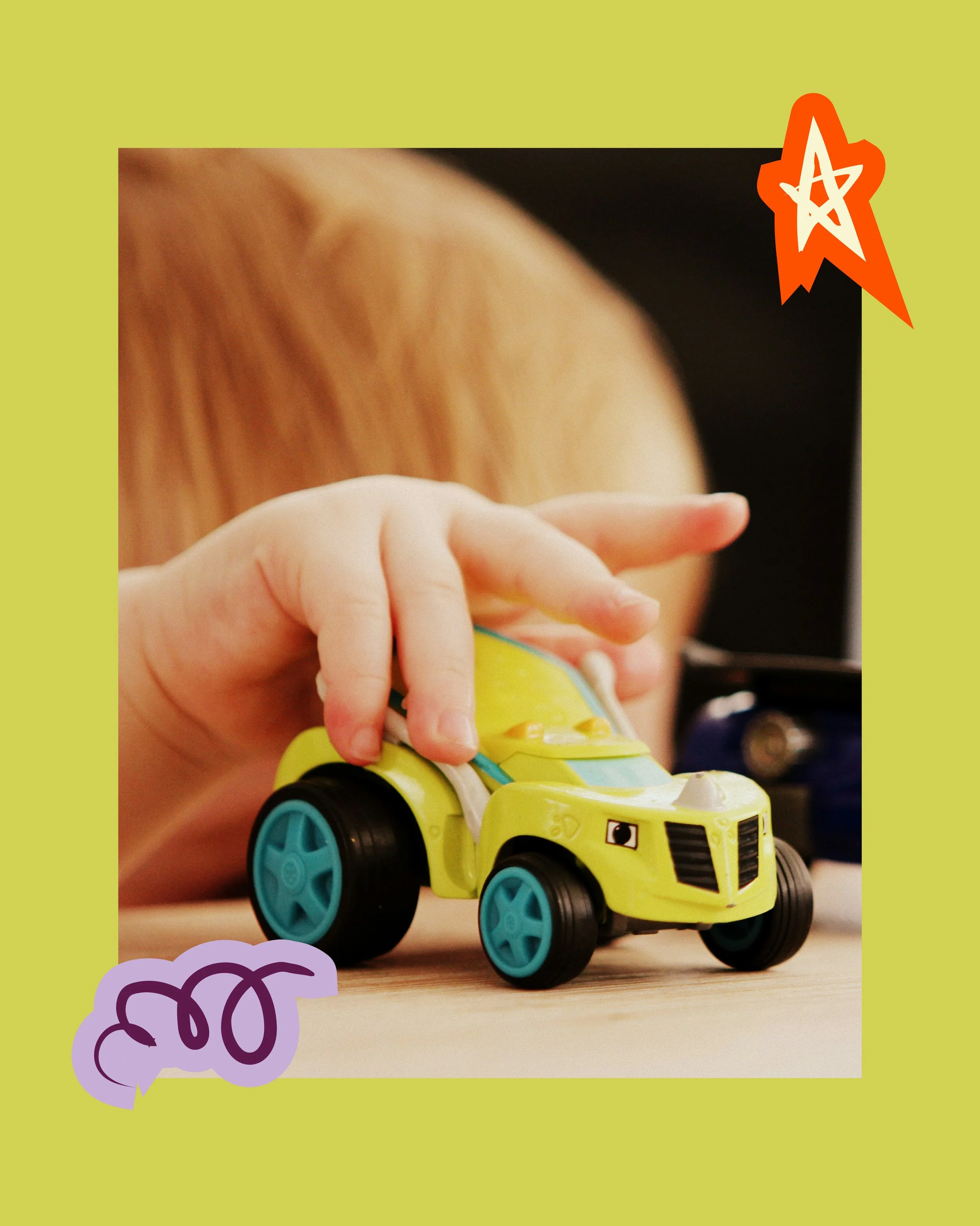 Close-up of a child's small hand playing with a toy yellow car on a wooden surface, with part of the child's arm, hair, and a black background visible.