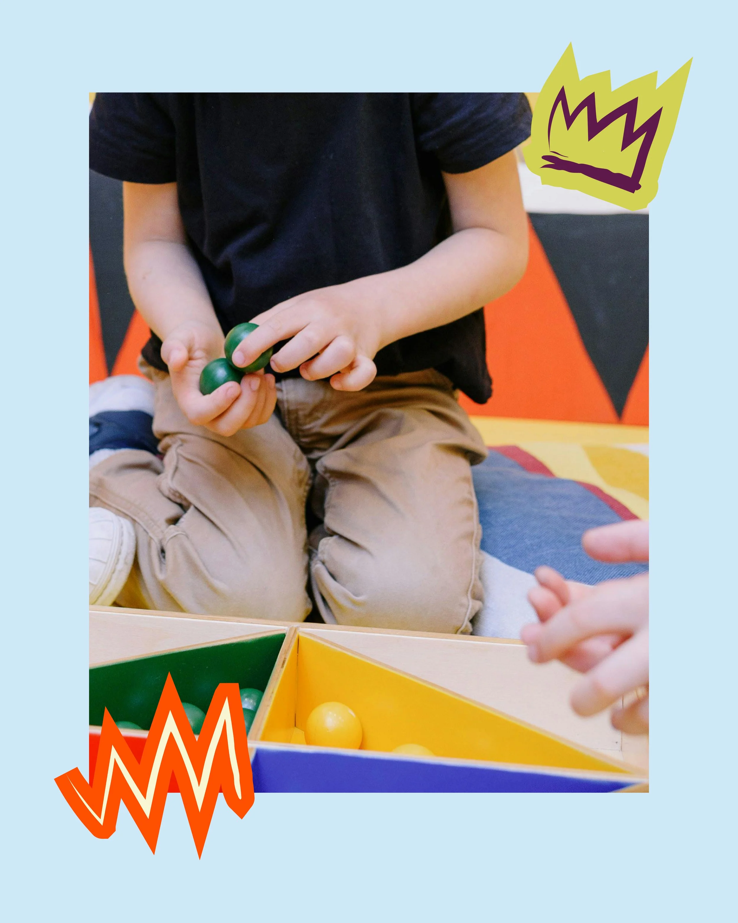 Close-up of a child's hands holding green balls near a colorful game box at an indoor play area.