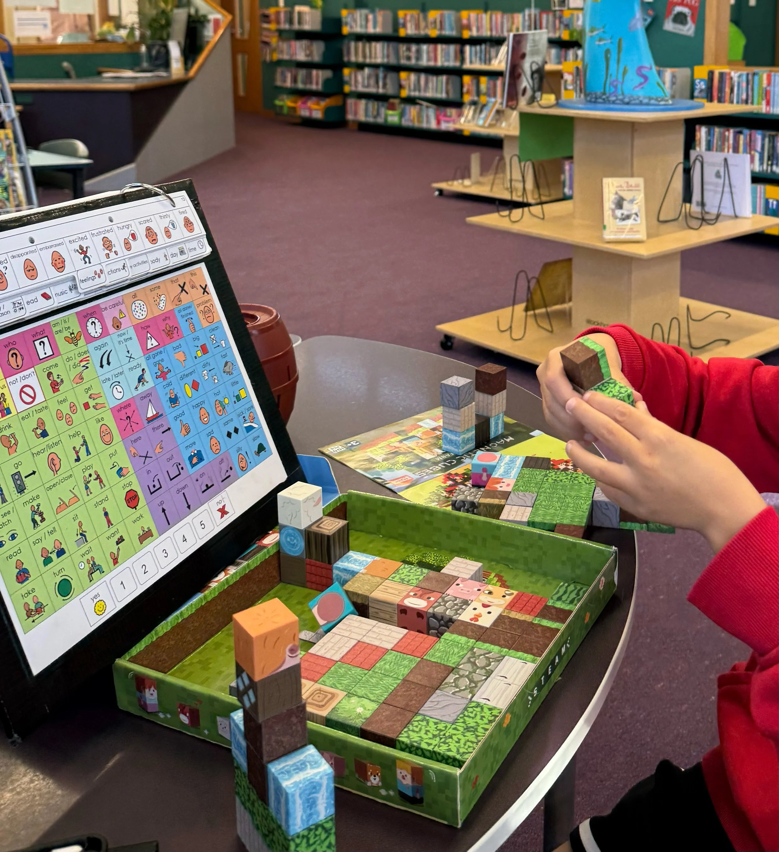 A children's library or bookstore with a display of various wooden blocks and books, and a colorful picture on the wall.