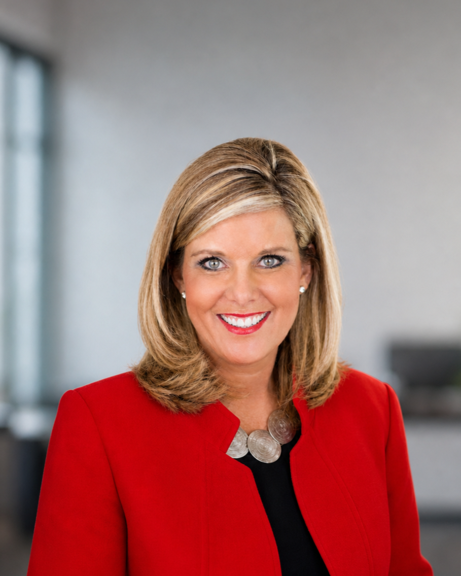 A woman with blonde hair, wearing a red blazer and a silver necklace, smiling in an indoor setting.