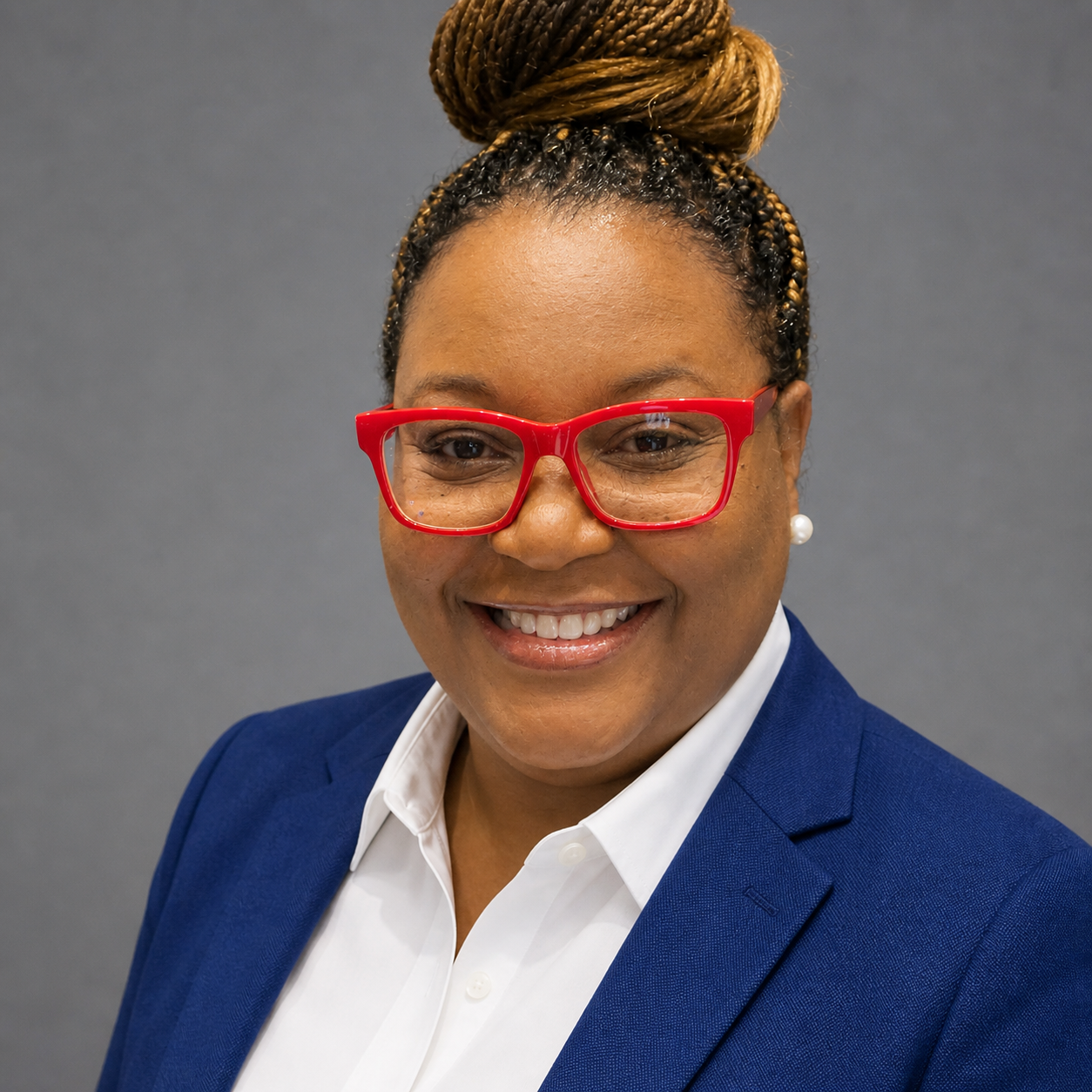 Professional woman wearing red glasses, pearl earring, blue blazer, and white shirt, smiling against a gray background.