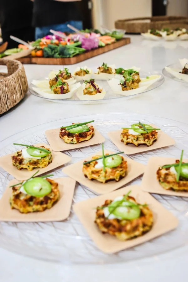 Appetizers on a glass tray with small round vegetable tarts topped with a green garnish.