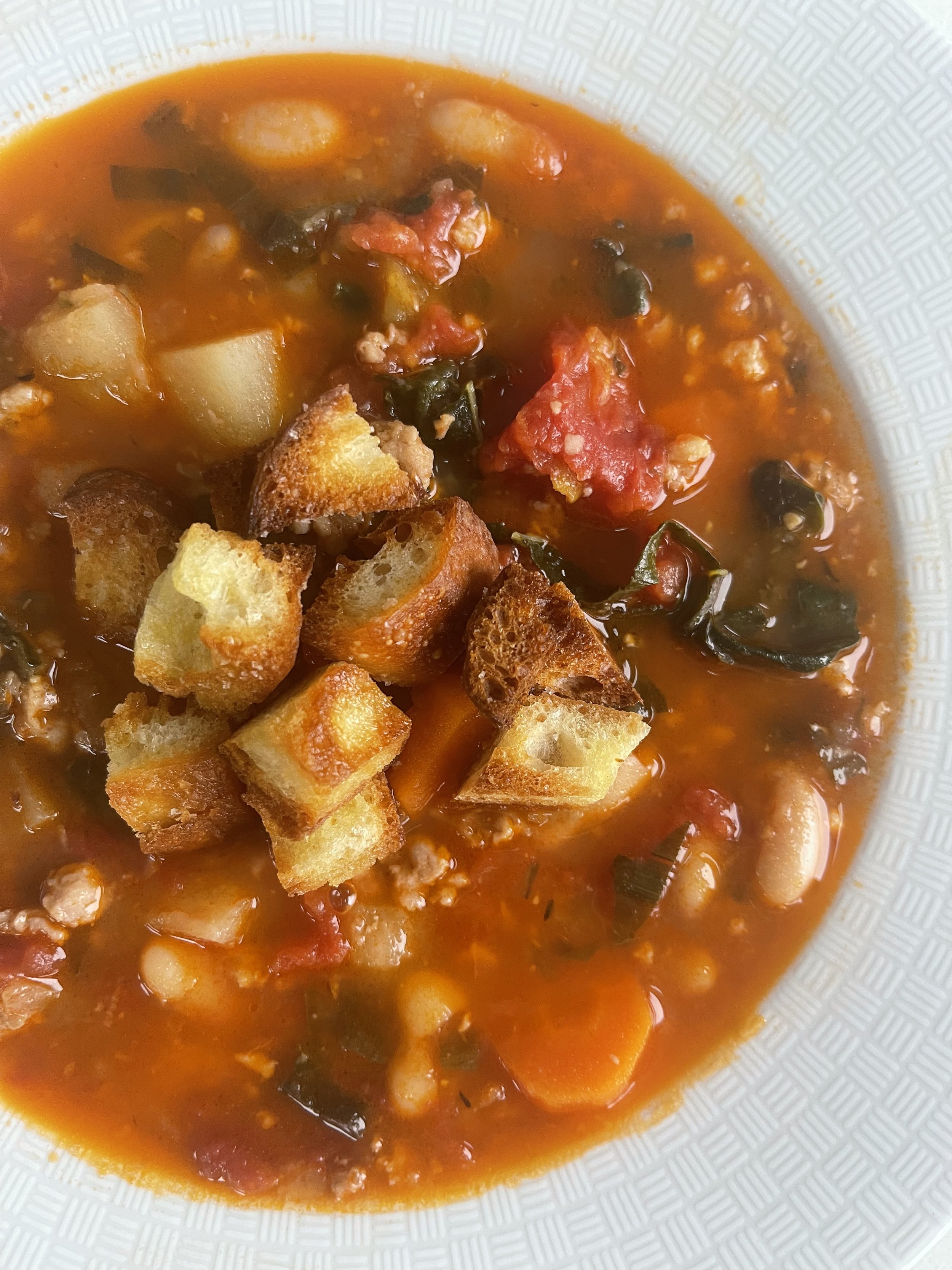 Soup with tomatoes, white beans, potatoes, and croutons in a white bowl also known as Ribollita Soup