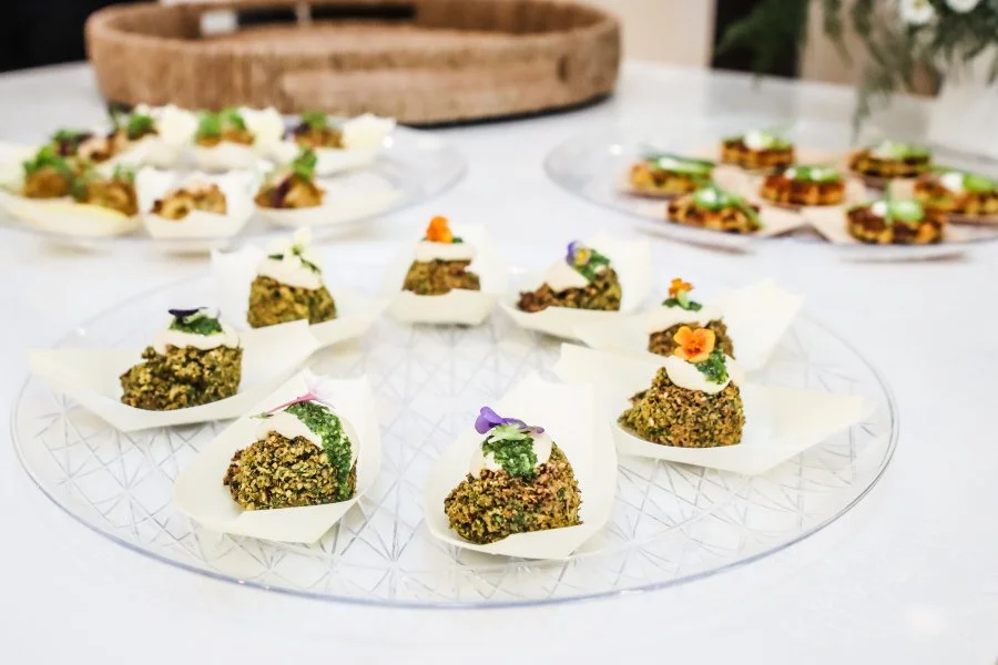 Assorted gourmet canapés on a clear glass platter with edible flowers and garnishes, with other appetizer plates in the background.