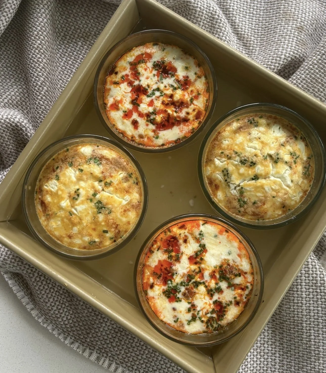 A tray holding five bowls of baked cheese and tomato-based dishes, garnished with herbs and spices.