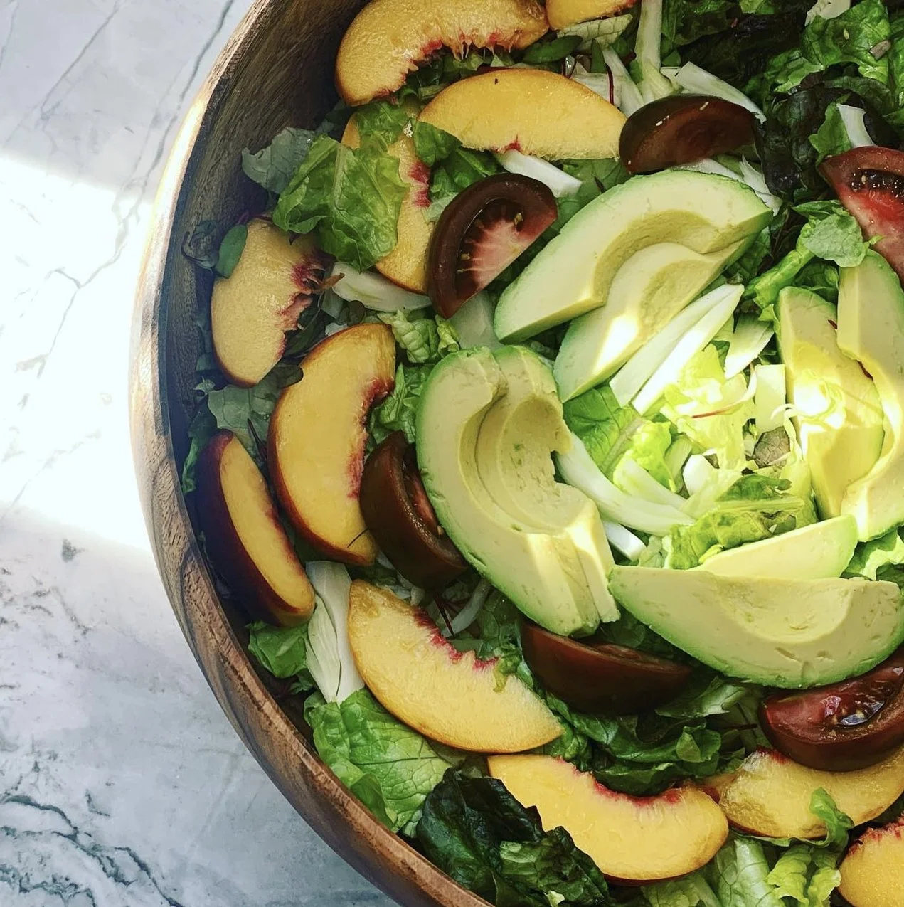 Mixed salad with sliced peaches, avocados, tomatoes, and greens in a wooden bowl