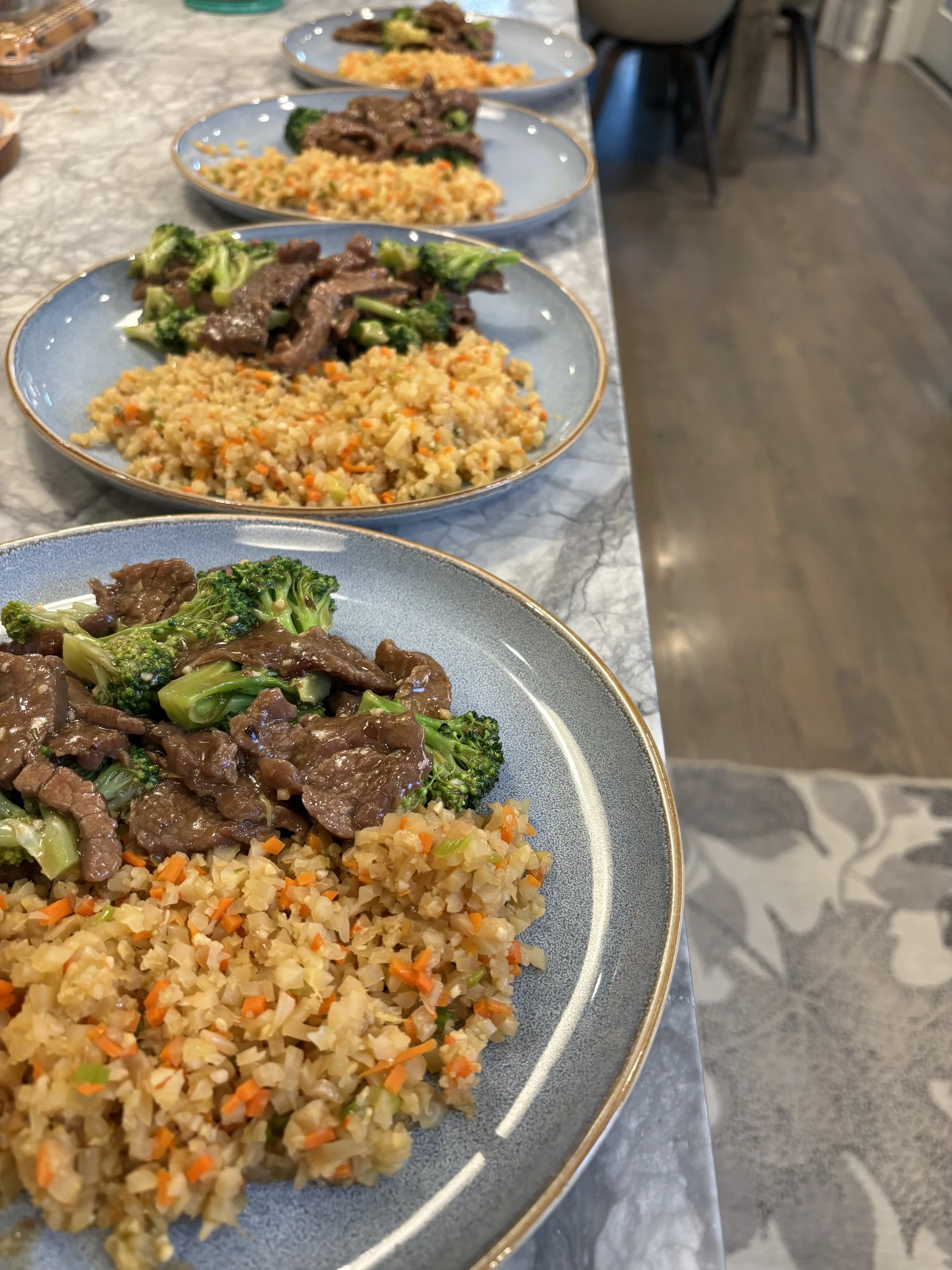 Multiple plates of food on a marble table, featuring stir-fried beef with broccoli, fried rice with mixed vegetables, and another dish in the background.