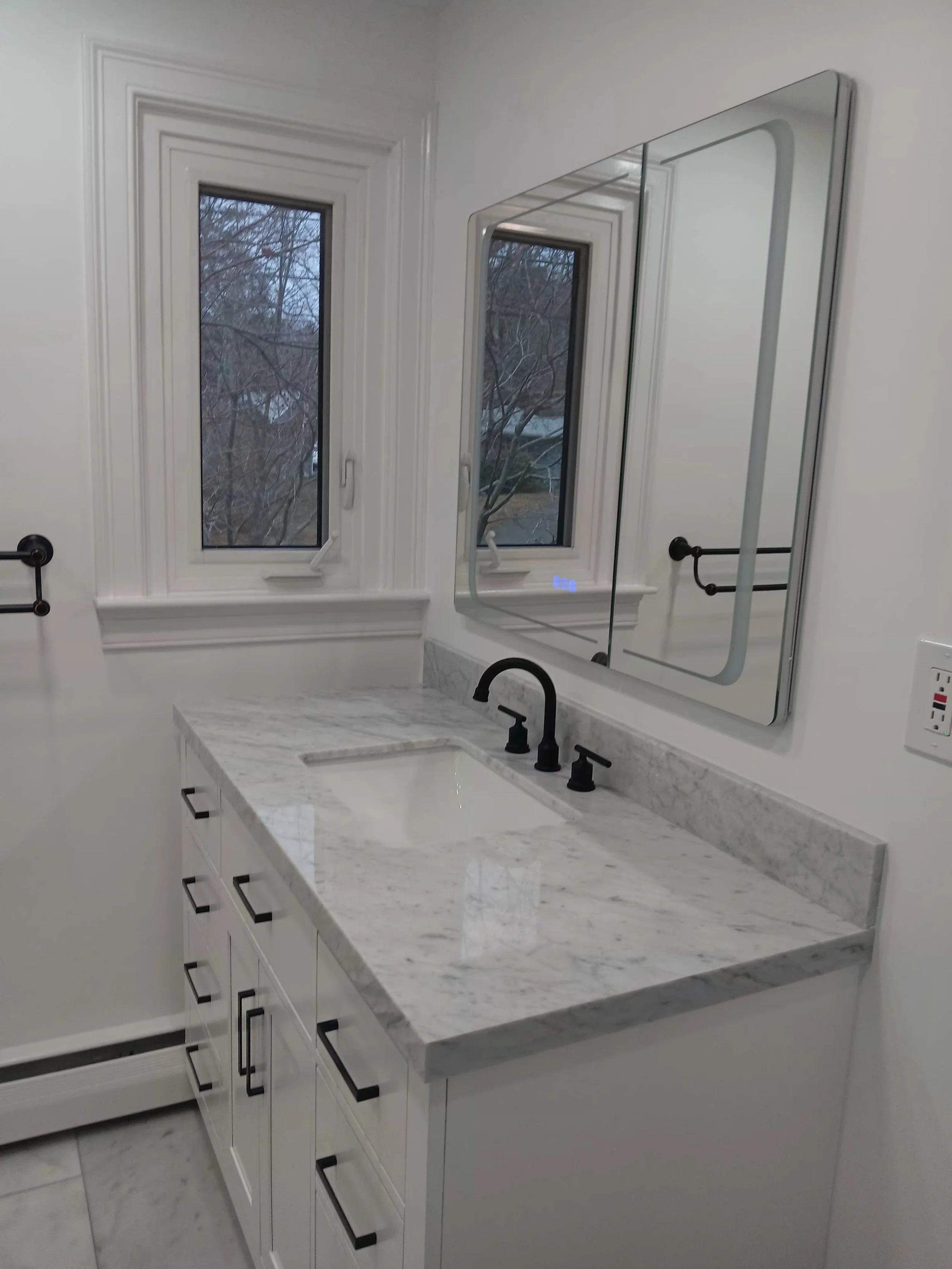 Bathroom with white cabinetry, a marble countertop, black hardware, two windows, and a mirror above the sink.