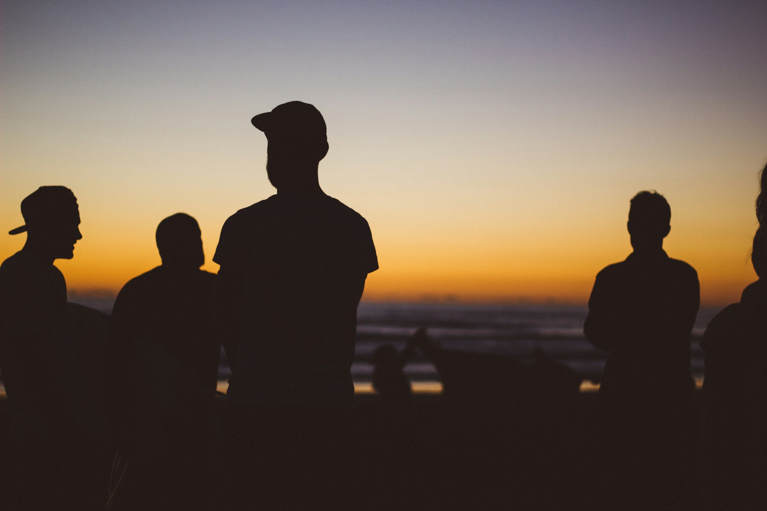 Silhouettes of five people standing together at sunset on the beach.