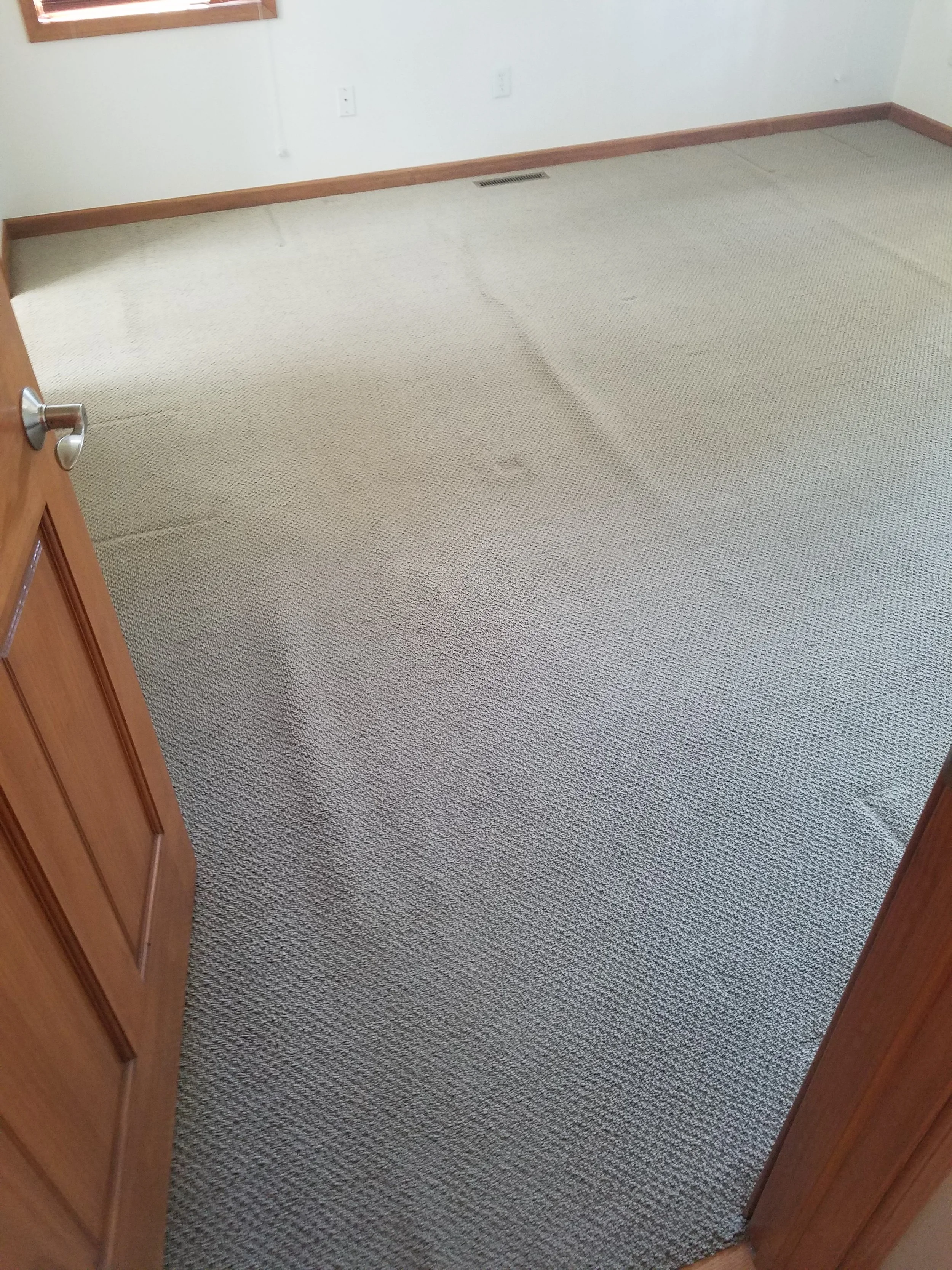 Empty room with beige carpet, wooden baseboards, white walls, and a window with wooden trim.