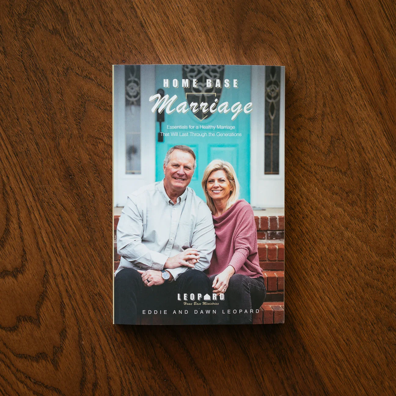 Book titled 'Home Base Marriage' featuring a smiling middle-aged man and woman sitting on steps in front of a house.