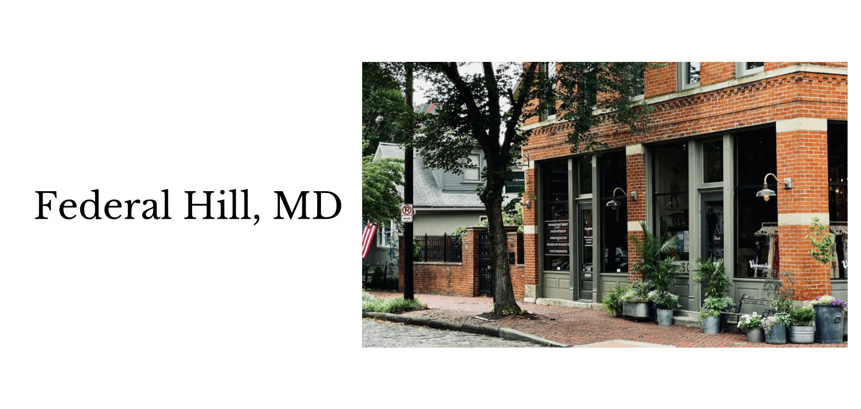 A storefront on a brick building with large windows, outdoor plants, and greenery on a city street in Federal Hill, MD.