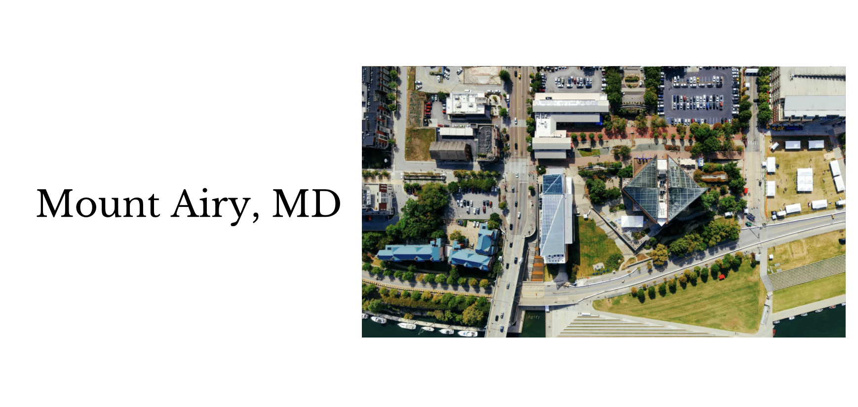 Aerial view of Mount Airy, Maryland, showing buildings, roads, parking lots, green spaces, and a bridge over water.