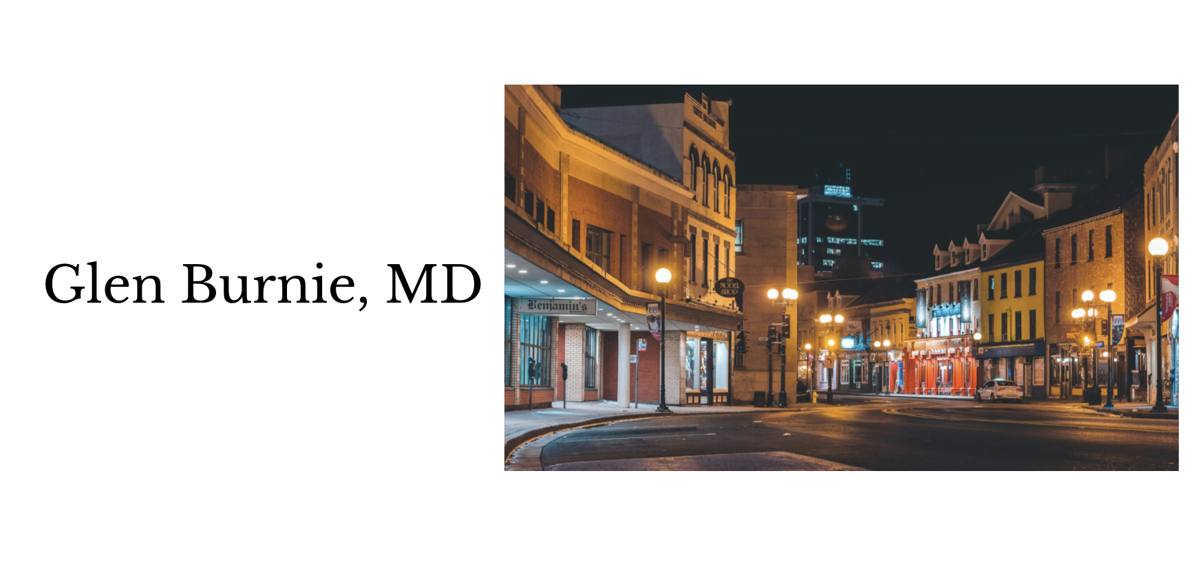 Nighttime view of downtown Glen Burnie, MD with lit street lamps and historic buildings on a quiet street.