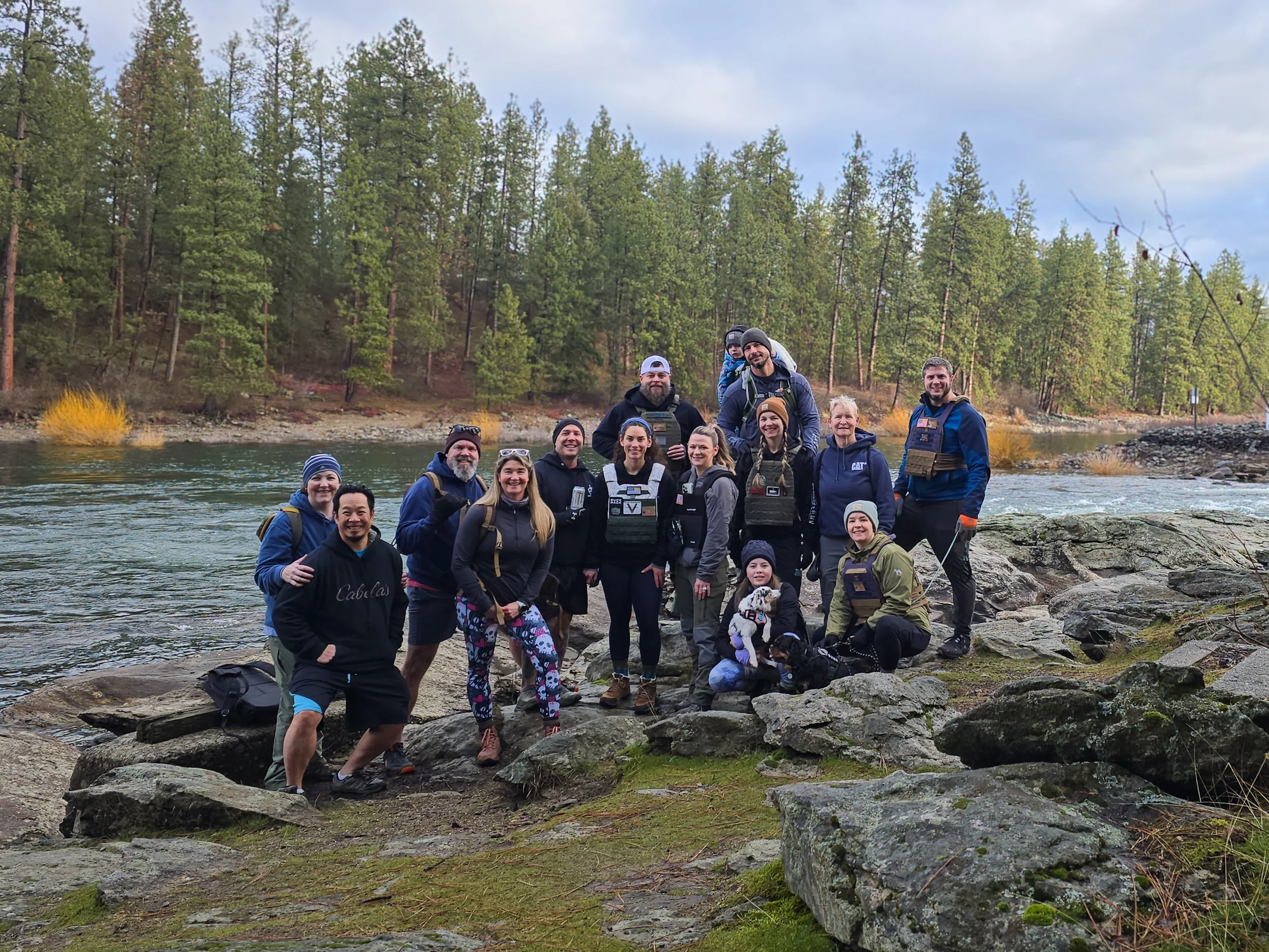 A group of people gathered on rocks beside a river in a forested area during daytime, smiling and posing for a photo.