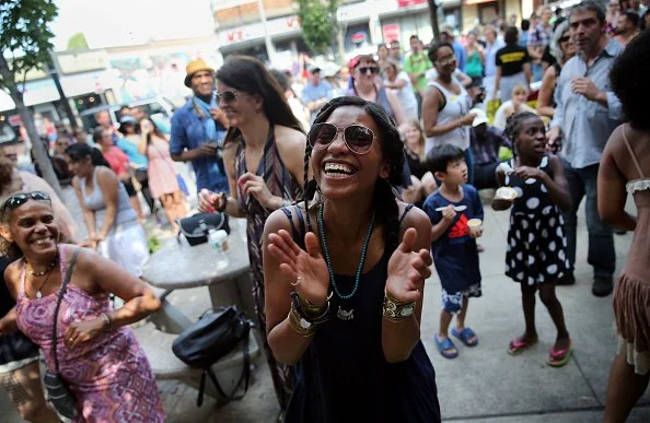 A group of people, including women and children, smiling and enjoying themselves at an outdoor event in a busy urban area.