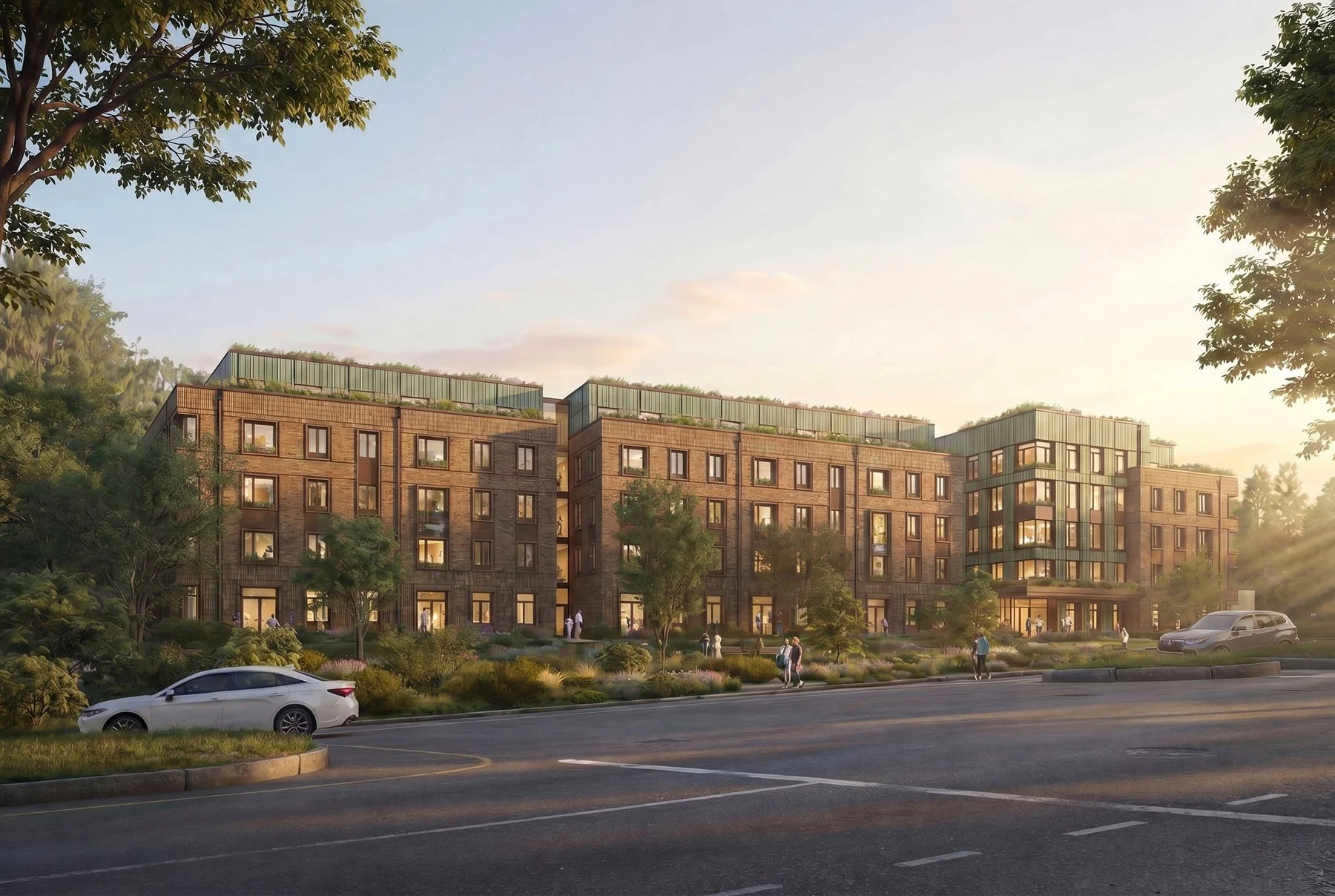 A modern residential building complex with multiple stories, large windows, green rooftops, and surrounding trees, with people walking outside during sunset and a few cars parked along the street.
