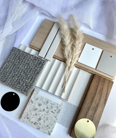 Arrangement of home decor and interior design samples including wood, tile, fabric, a dark circular object, a small mirror, a faux plant, and a gold round object.