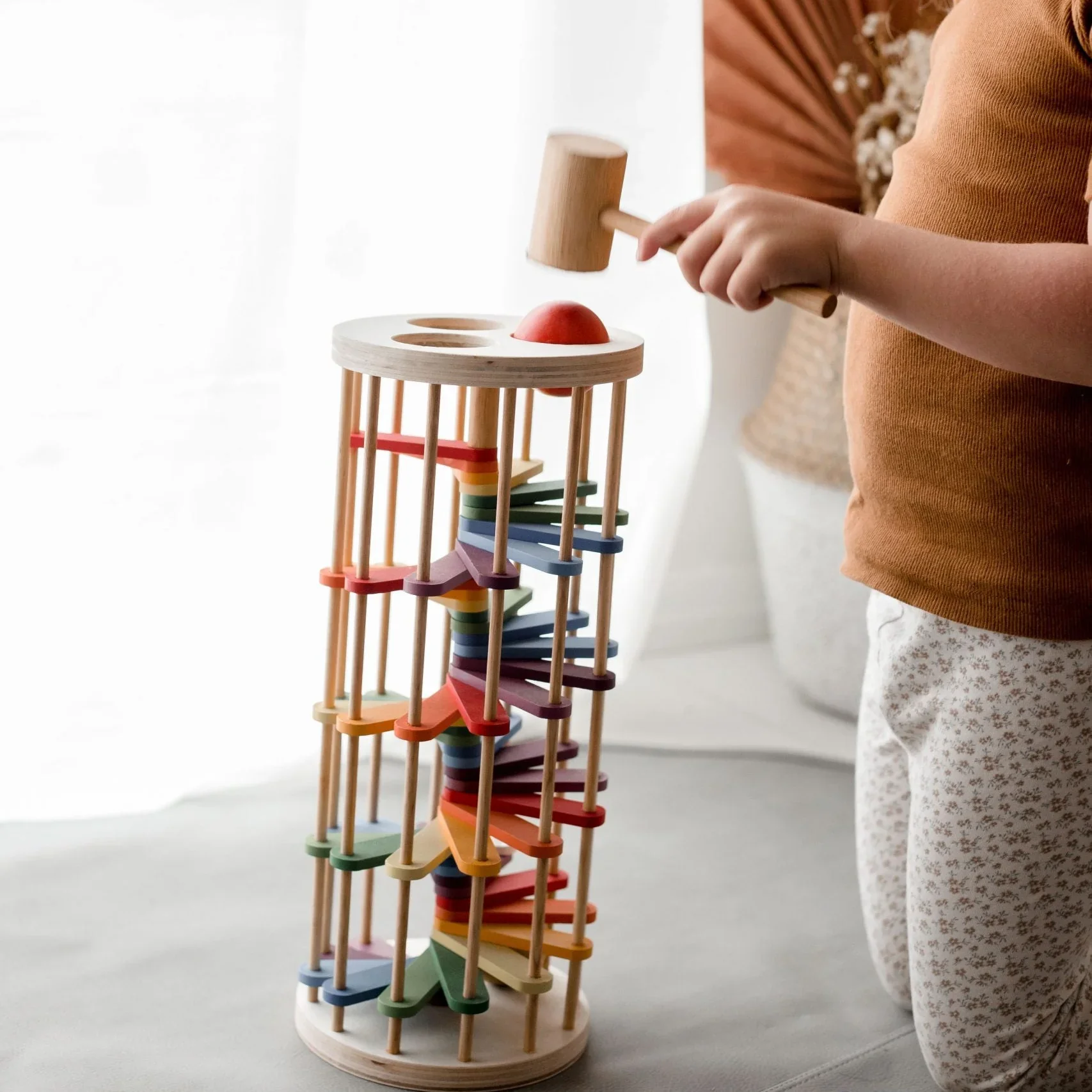 A child wearing patterned pants and an orange shirt playing with a colorful wooden marble run.