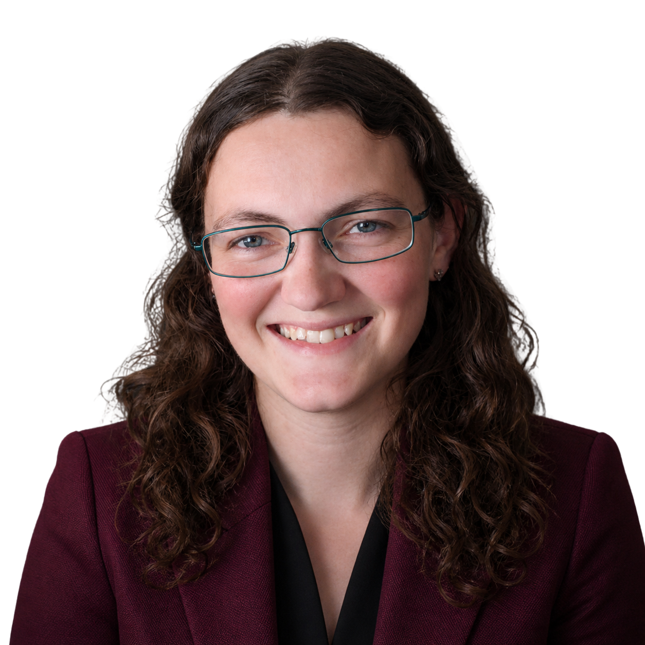 A woman with long, curly brown hair, glasses, and a burgundy blazer smiling at the camera.