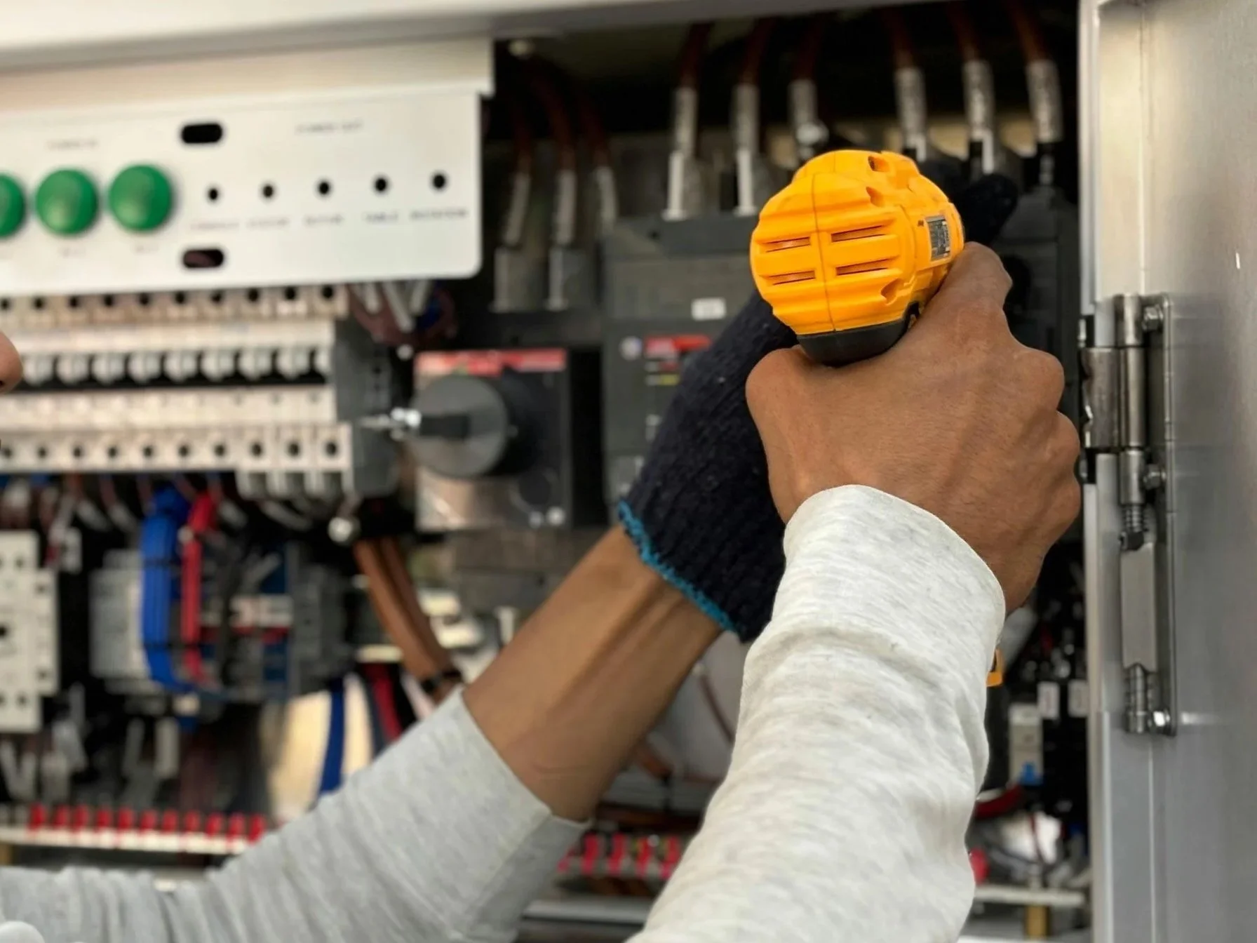 A person using a yellow cordless drill to work on electrical panel inside an electrical cabinet.