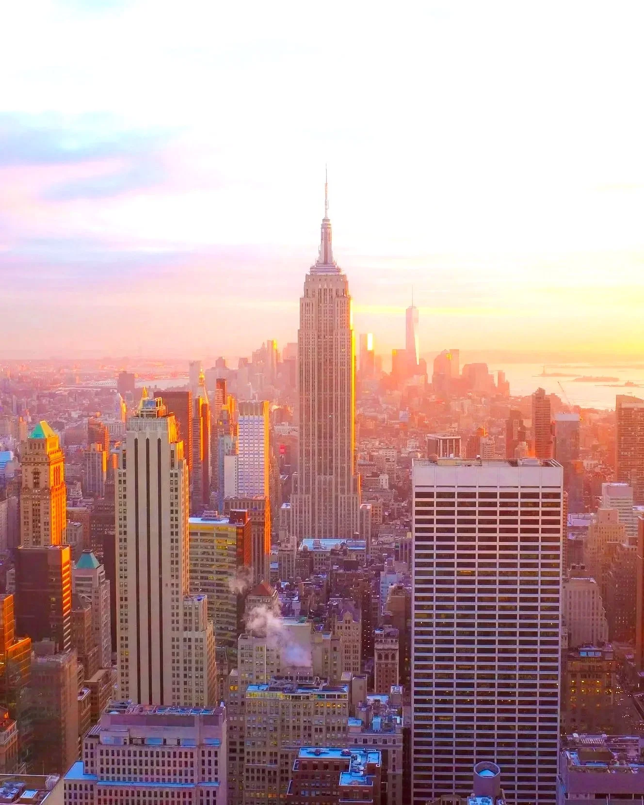 Sunset over Manhattan skyline with the Empire State Building in the center and One World Trade Center in the background.