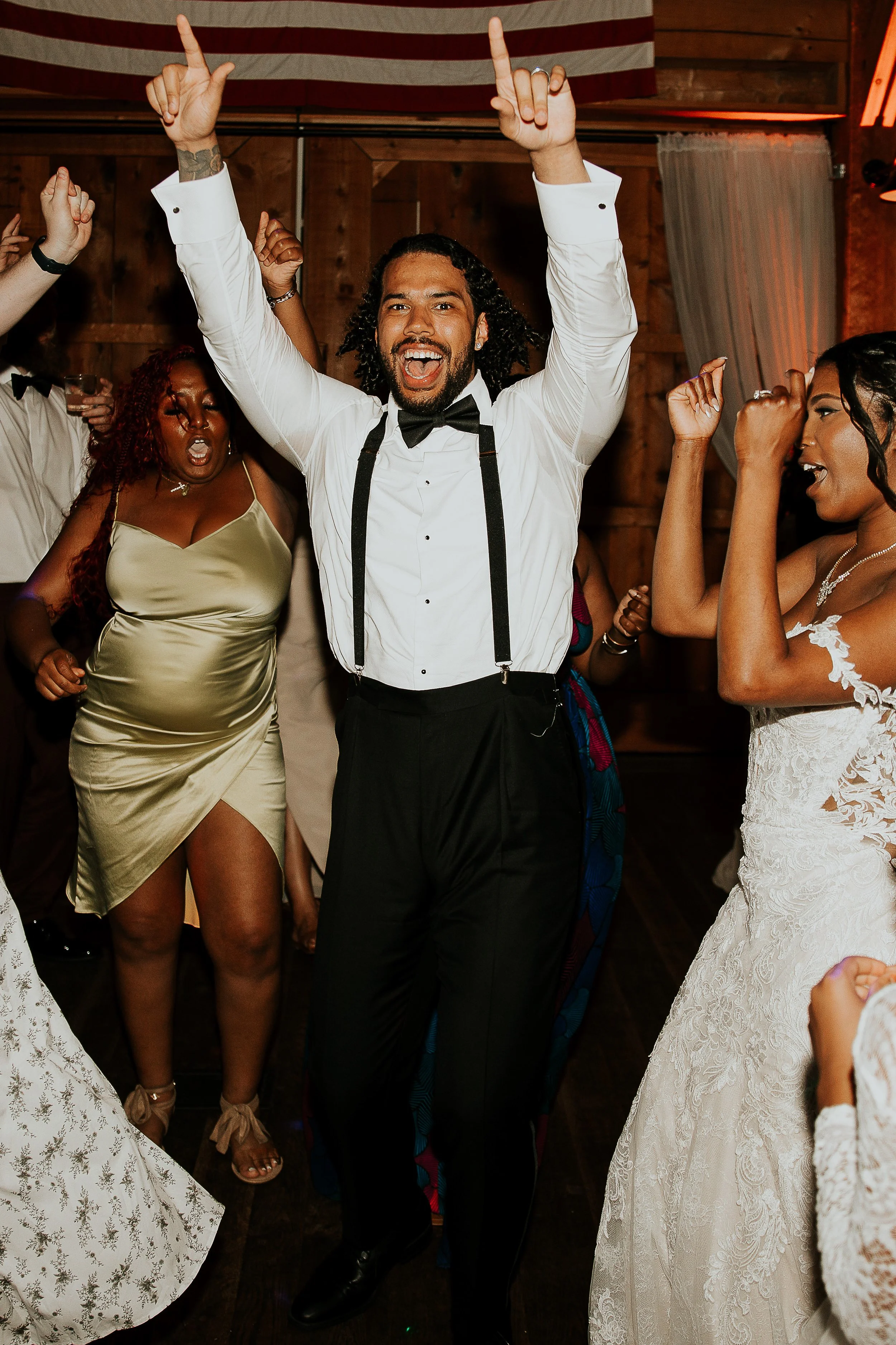 People dancing and celebrating at a party, with a man in a tuxedo with suspenders in the center.