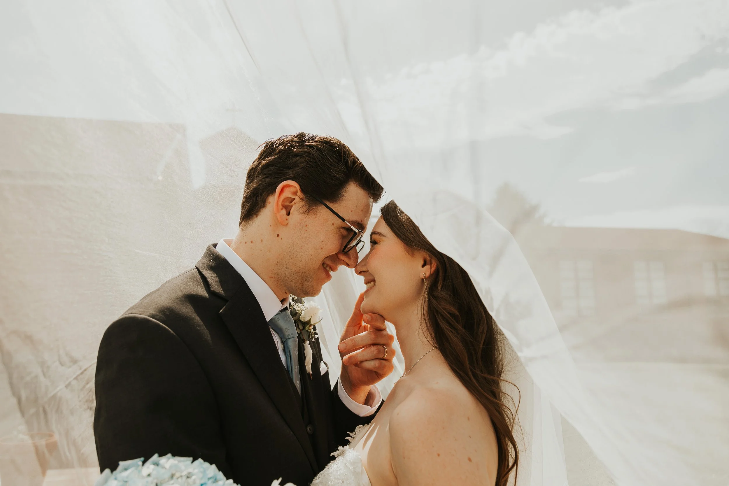 A newlywed couple sharing a tender moment under a wedding veil.