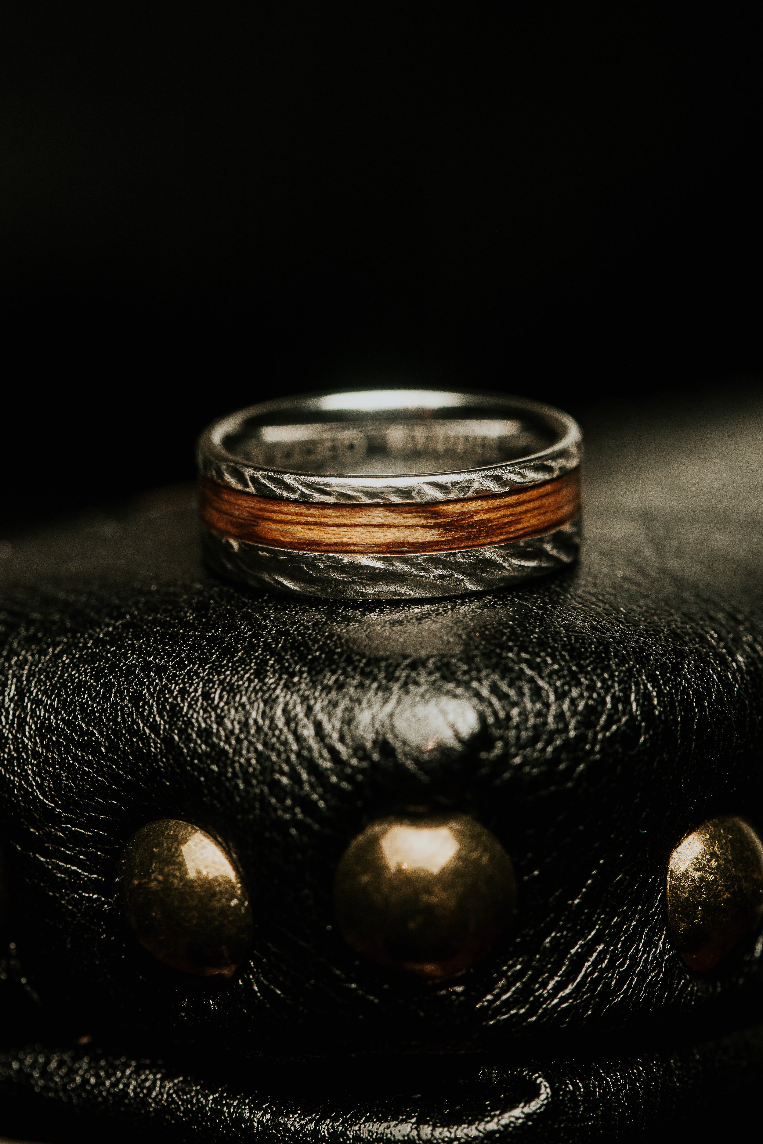 Close-up of a silver ring with a copper band, resting on a black textured surface with gold spherical accents in the foreground.