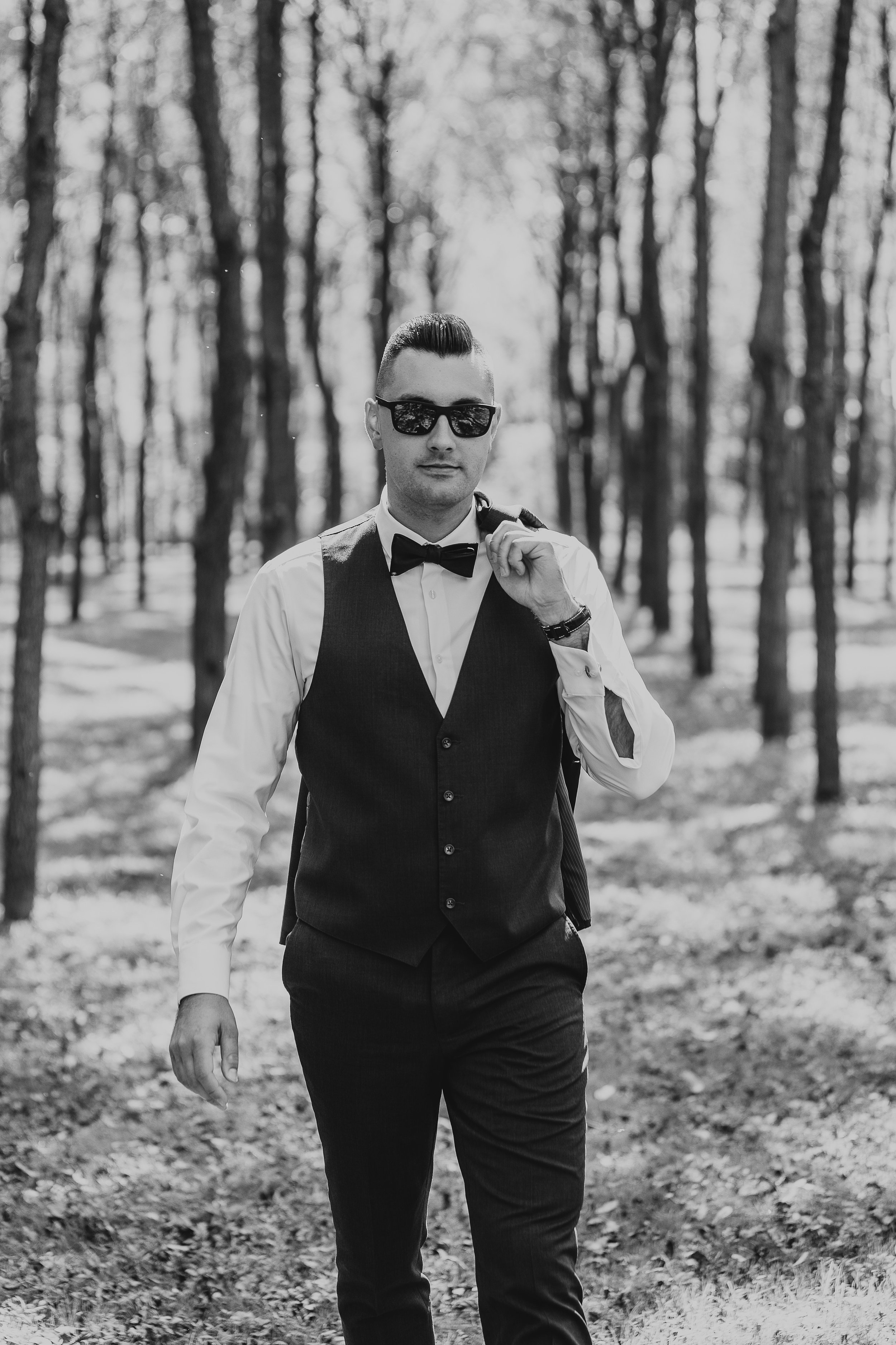 A man in a suit with sunglasses walking in a wooded area.