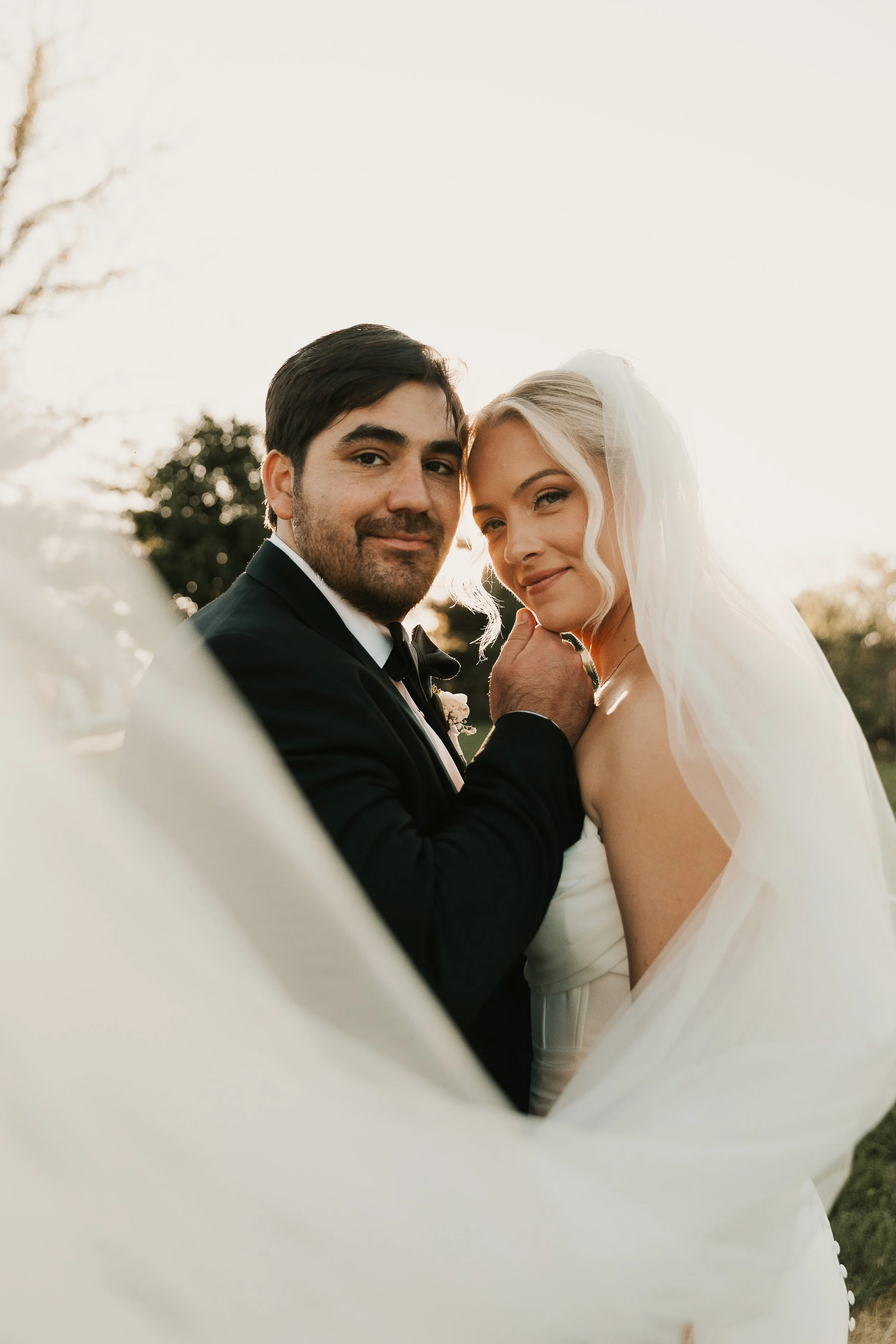 A bride and groom sharing a close, intimate moment outdoors during sunset.