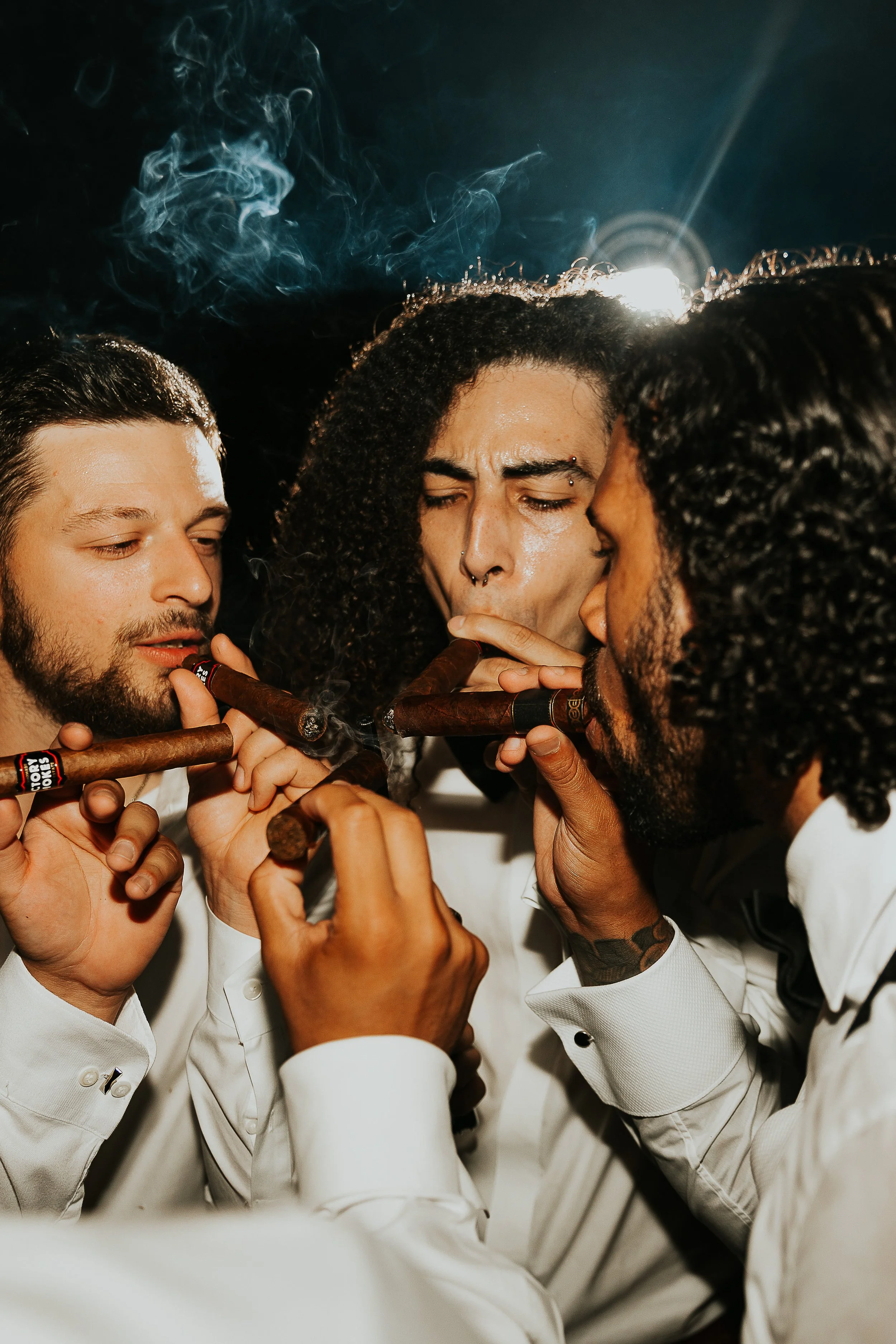 A group of four men, dressed in white chef coats, gathered closely together, sharing cigars and smoking in unison.
