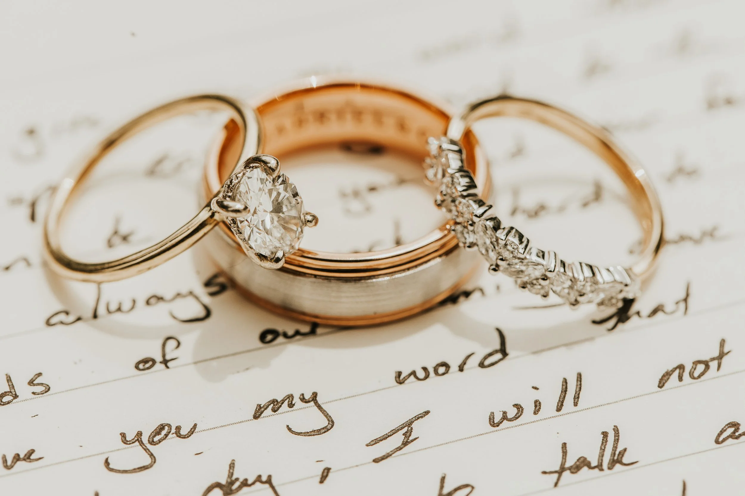 Close-up of three wedding rings with gemstones, placed on handwritten paper with cursive writing.