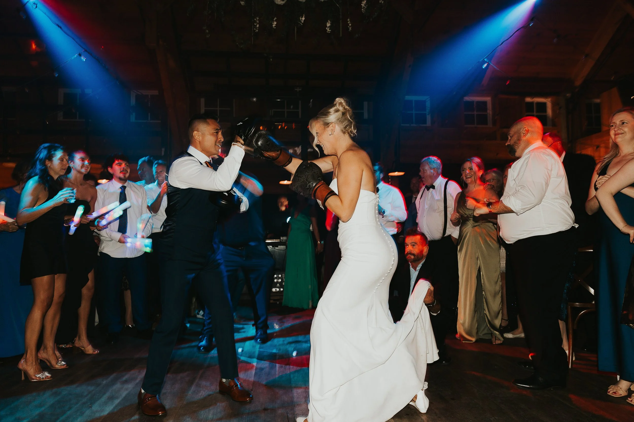 People dancing and socializing at a lively party or wedding reception in a wooden venue with colorful lighting.
